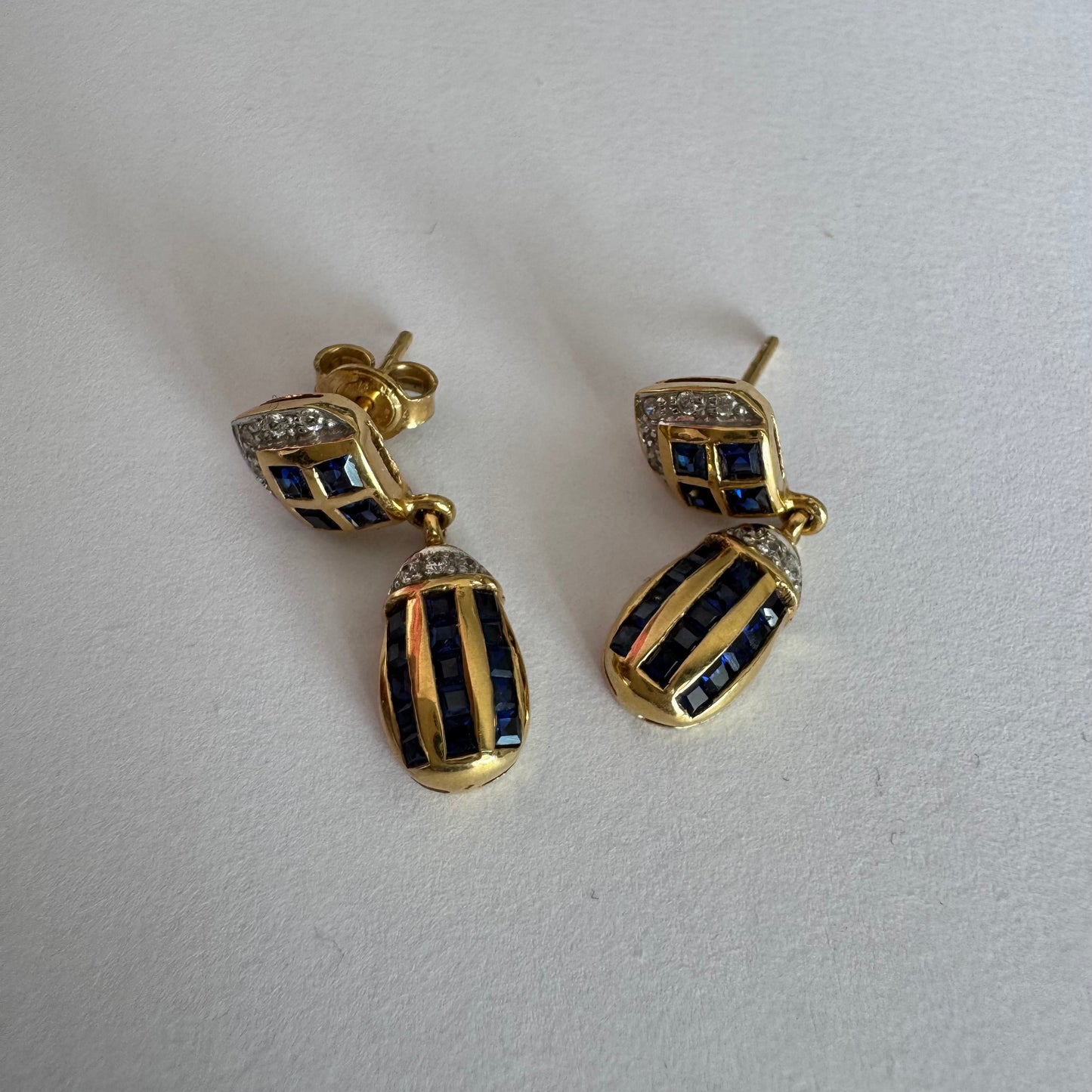 עגילי זהב צהוב 18 קראט תלויים, משובצים אבני ספיר כחולות בגוון כחול עמוק בעיצוב גיאומטרי, בשילוב יהלומים מנצנצים