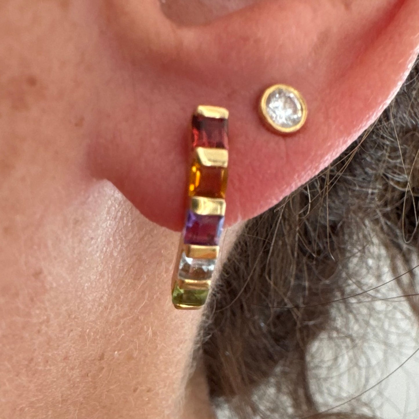 18K gold hoop earrings set with a vibrant line of multi-colored gemstones — including Garnet, Citrine, Amethyst, Peridot, and Blue Topaz.