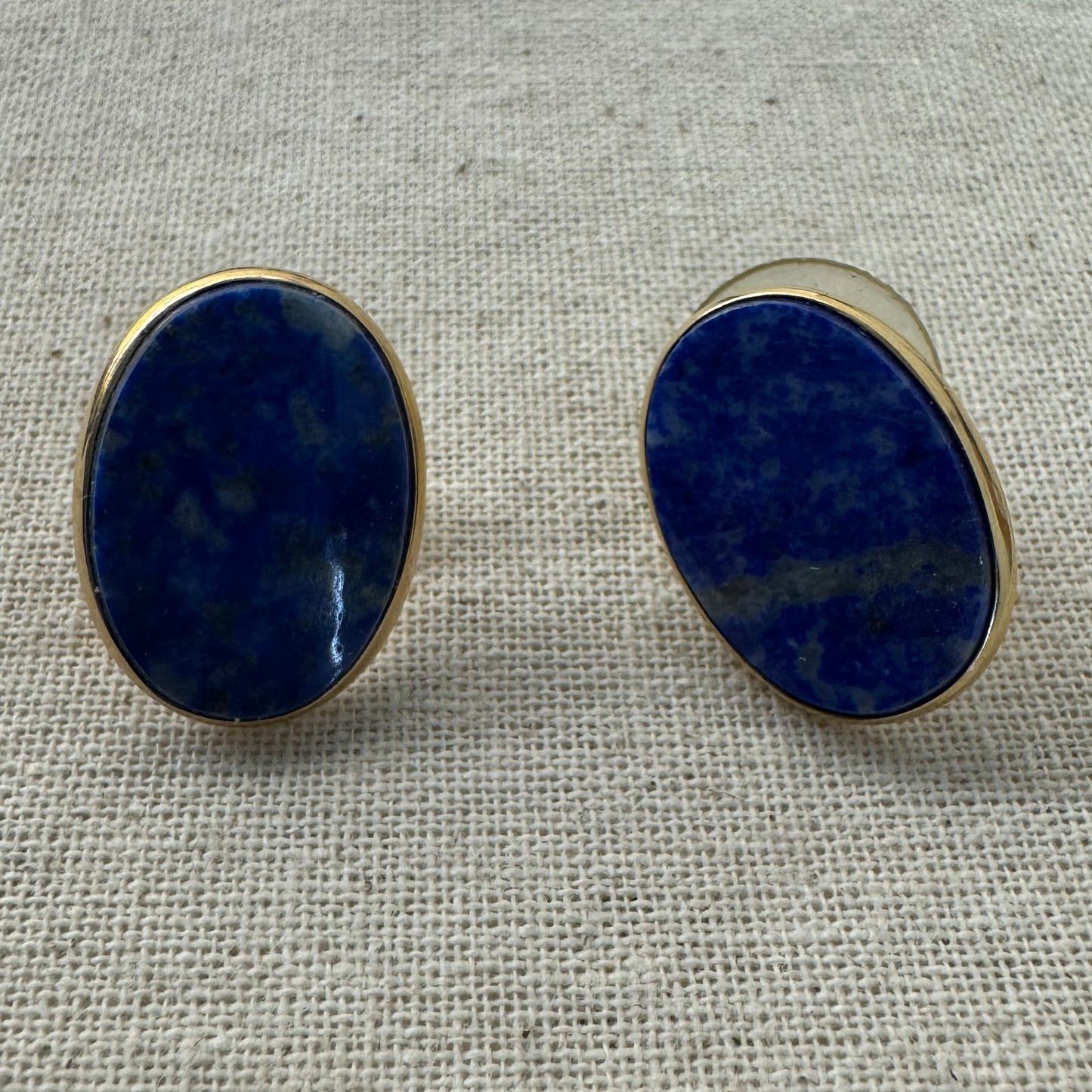 14K gold stud earrings set with polished oval Lapis Lazuli stones in a sleek gold bezel setting.