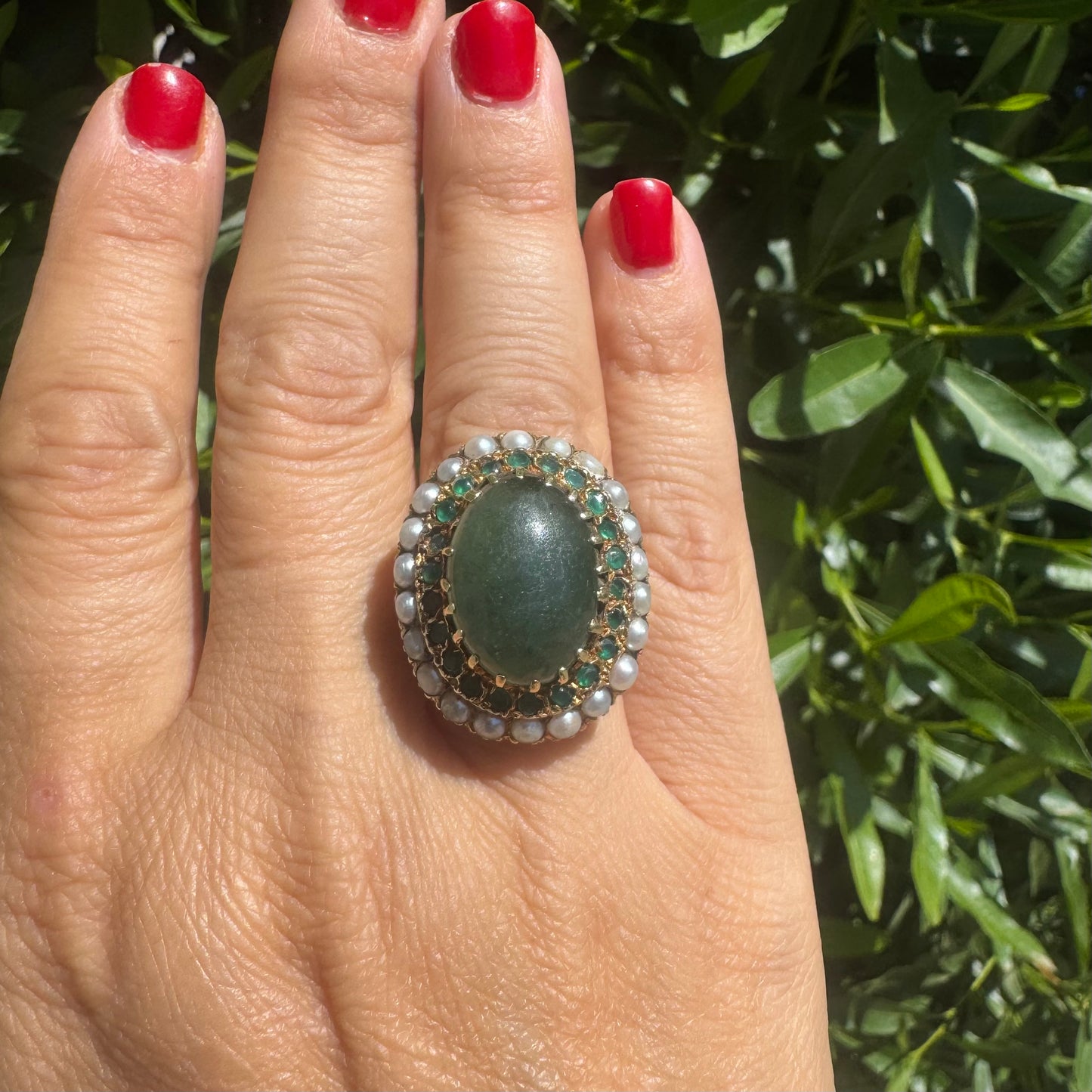 14K gold set with a large oval green Jade at its center, surrounded by concentric halos of sparkling Emeralds and delicate pearls