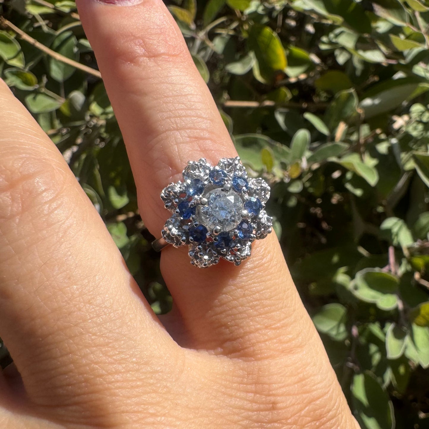 18K gold ring featuring a large round Diamond at the center, surrounded by a floral halo of purple -blue Tanzanite and & Diamonds.