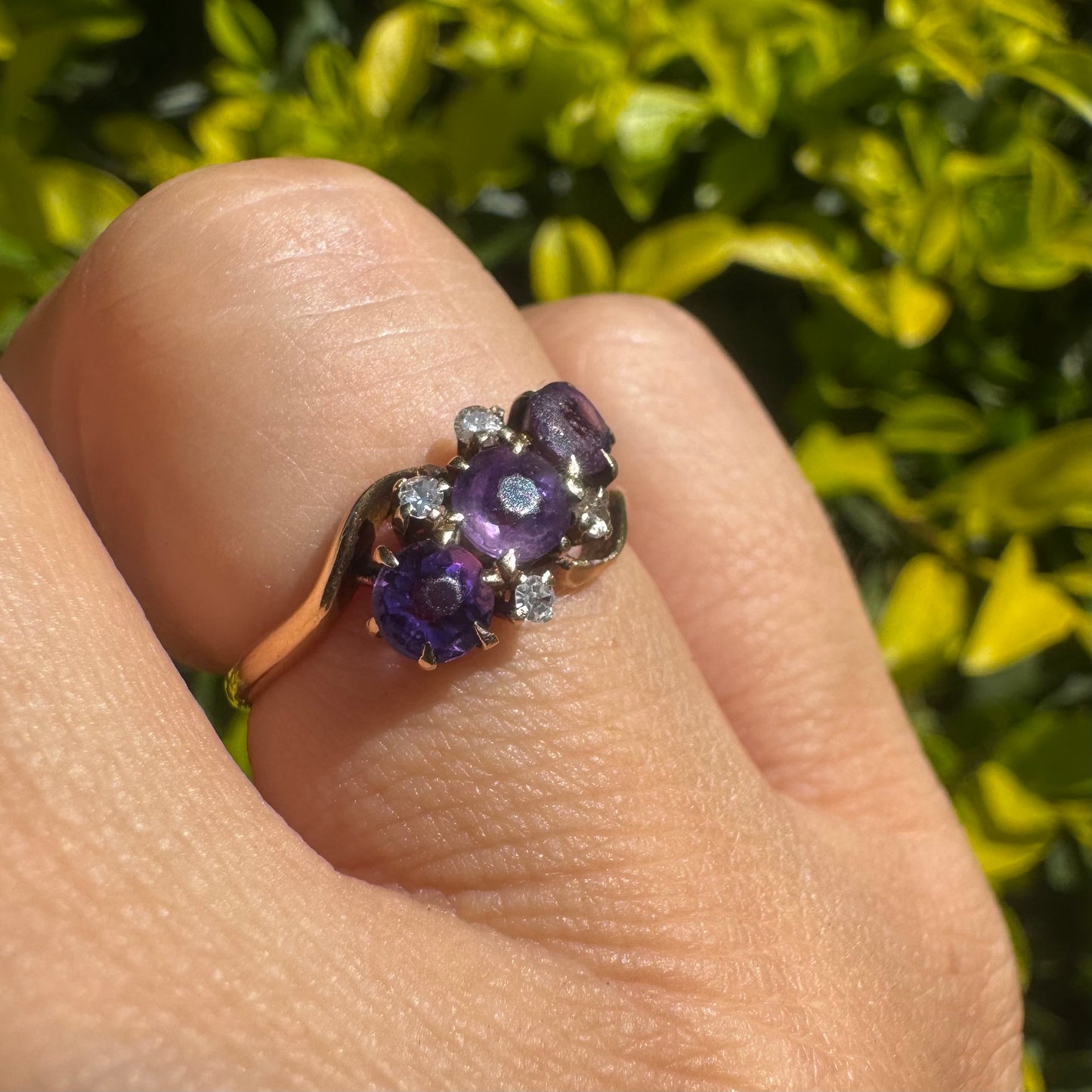 14K gold ring set with three round purple amethysts, accented by small sparkling Diamonds.