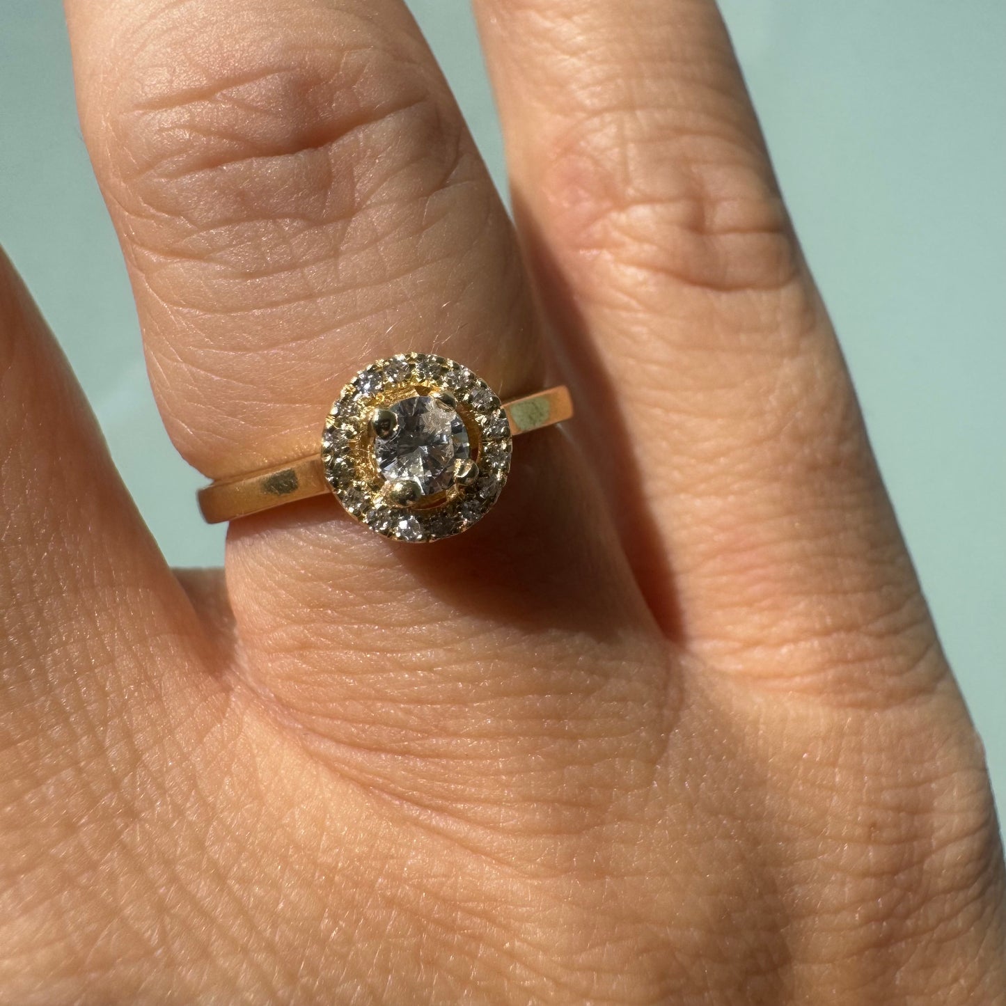 14K gold ring featuring a round central Diamond, surrounded by a sparkling halo of smaller Diamonds.