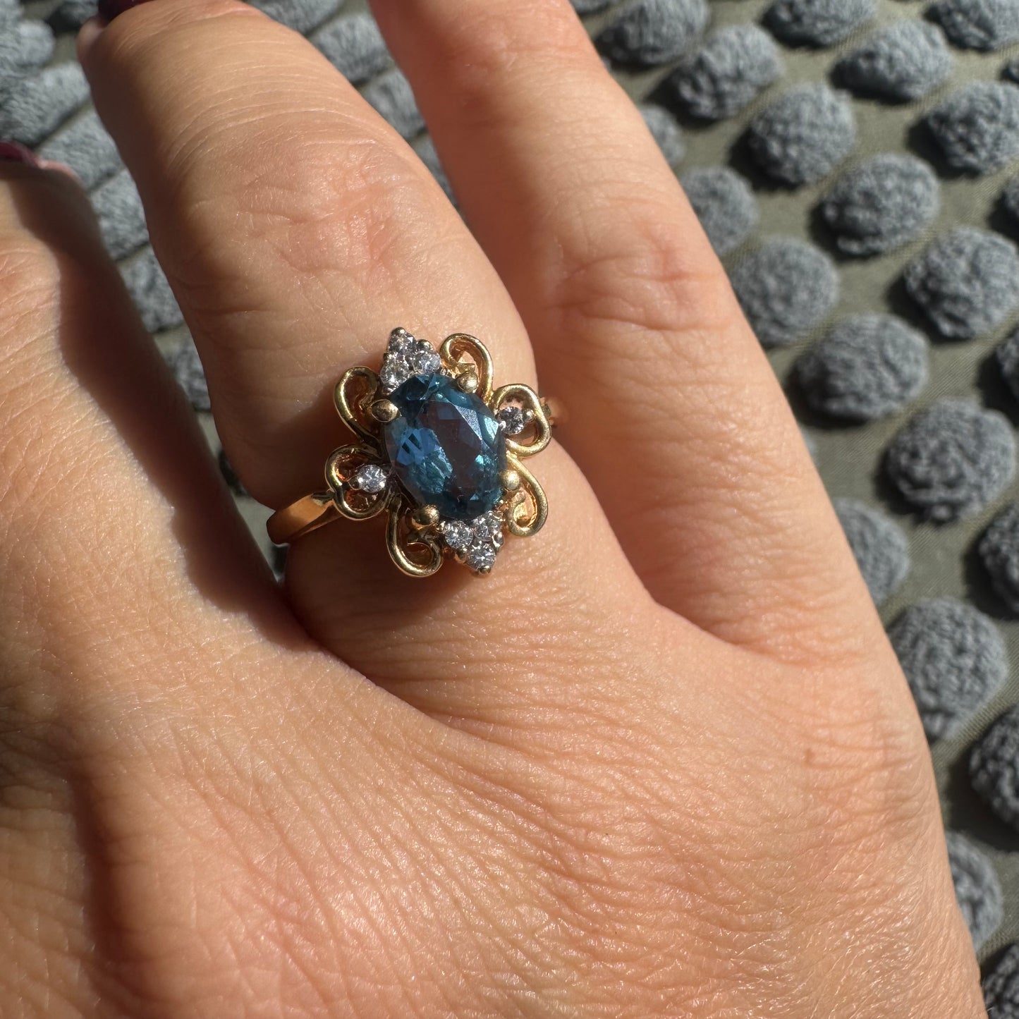 18K gold ring featuring an oval-cut Blue Topaz at the center, accented by sparkling side Diamonds and elegant scroll details.