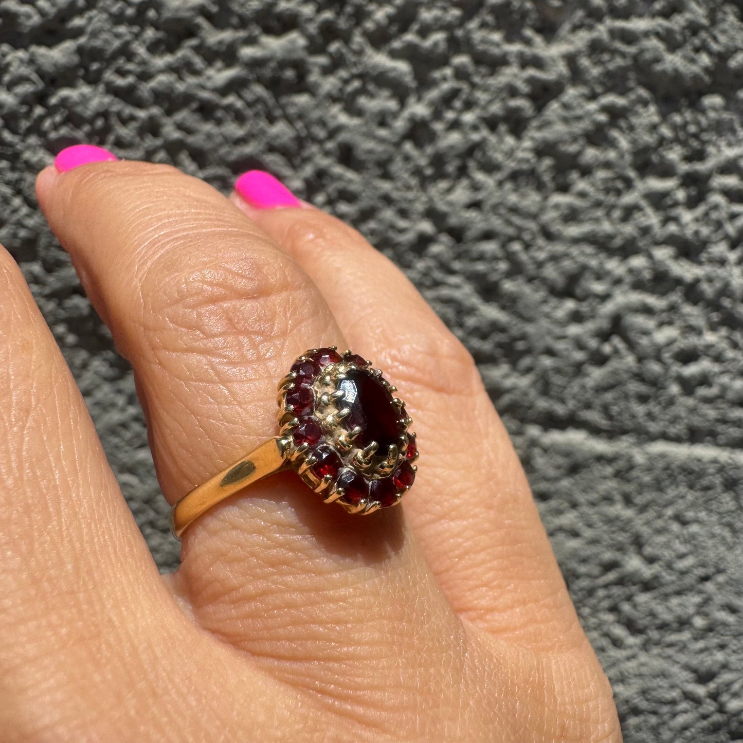 18K gold ring set with an oval garnet center stone, surrounded by smaller garnets