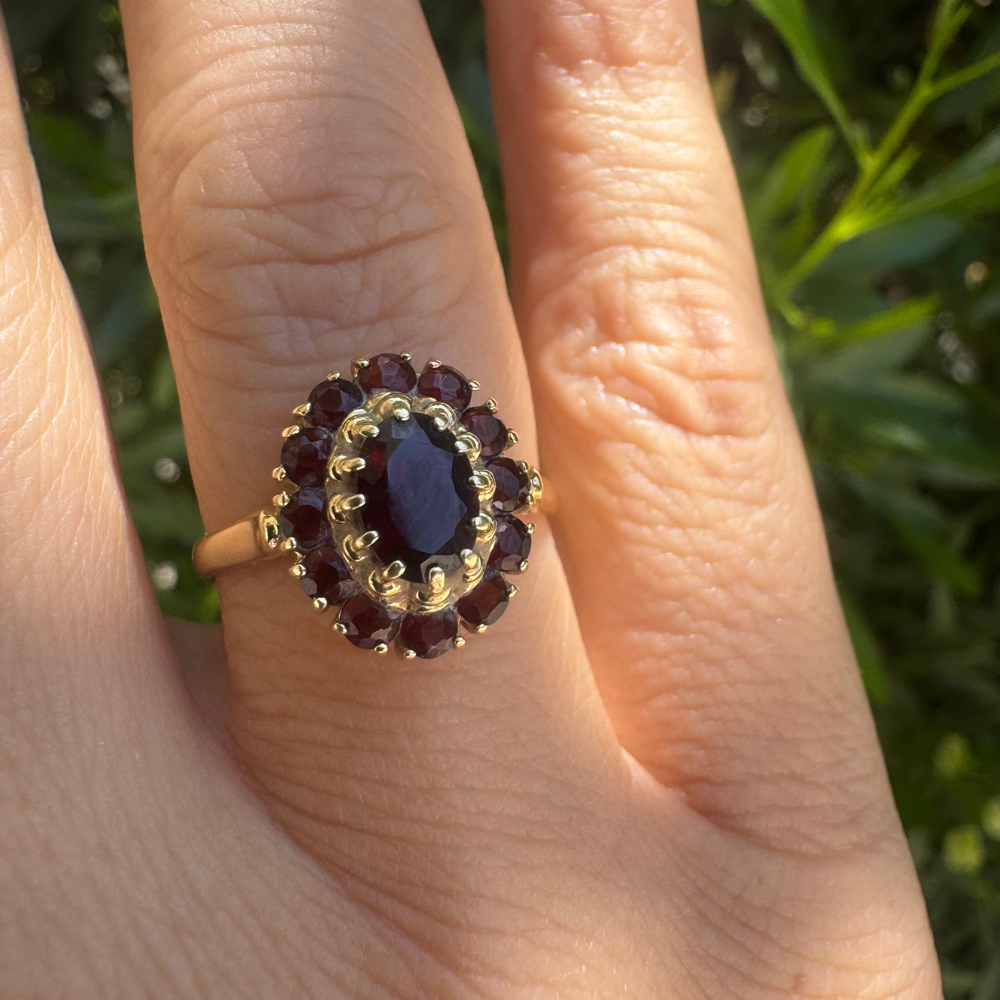 18K gold ring set with an oval garnet center stone, surrounded by smaller garnets