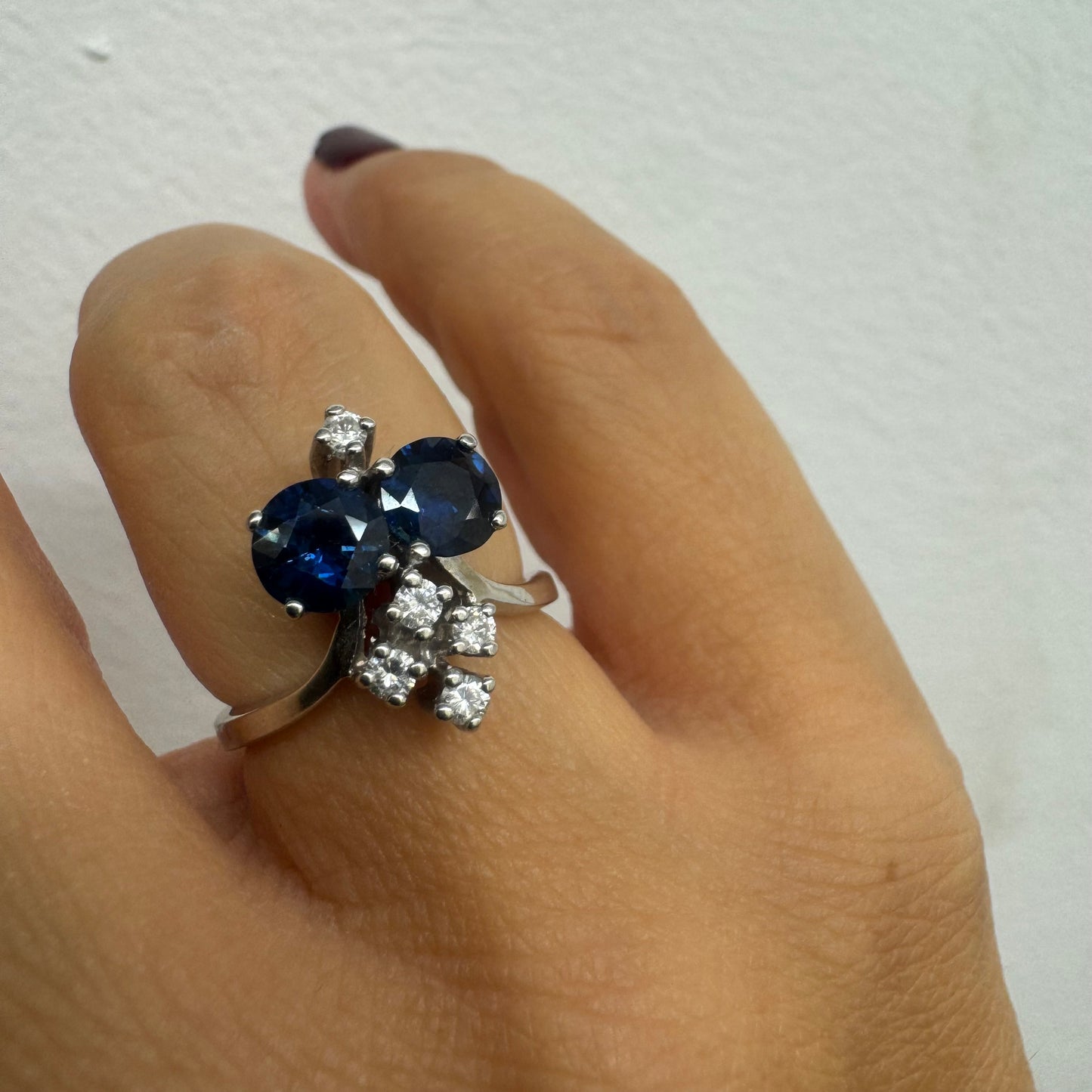 טבעת זהב לבן 14 קראט משובצת שתי אבני ספיר בגוון כחול עמוק ובאשכולות יהלומים לבנים מנצנצים.