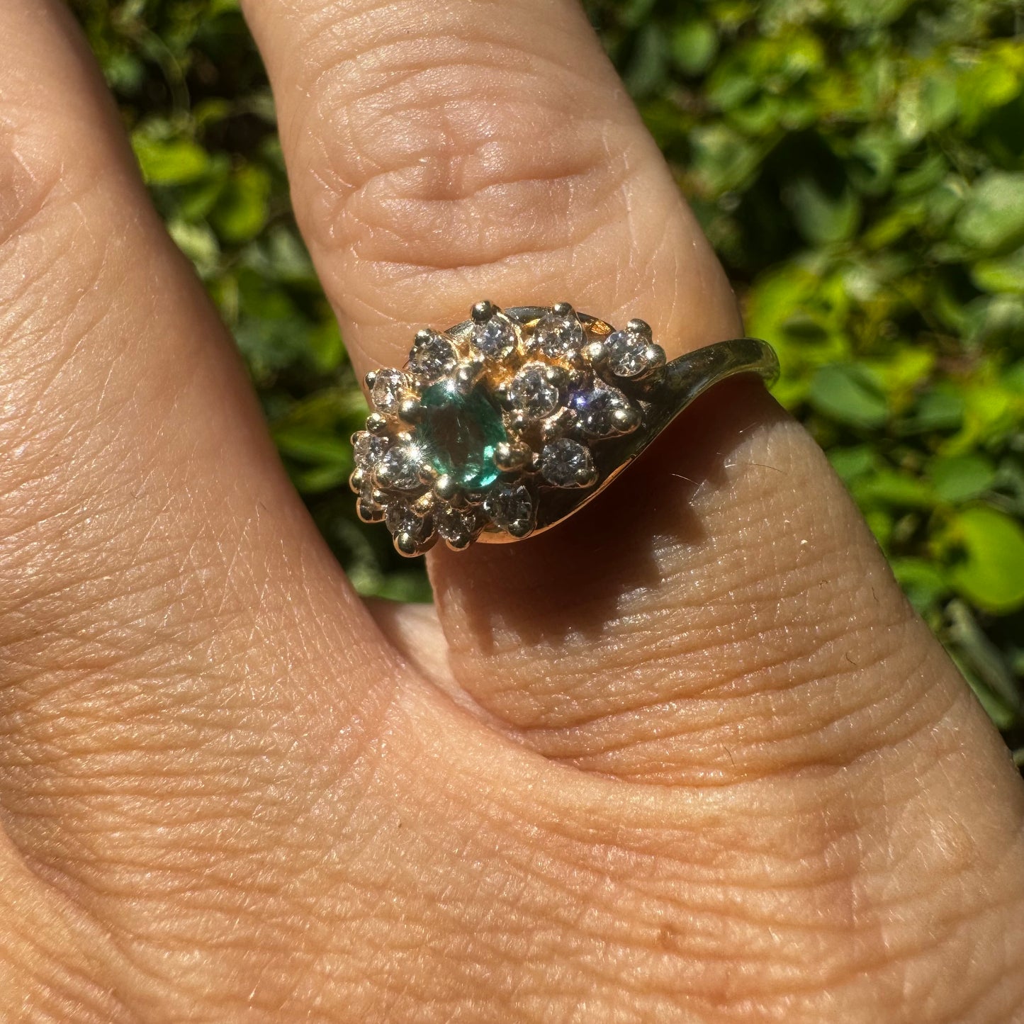 14K gold ring set with Emerald at its center, surrounded by a halo of brilliant-cut diamonds arranged in a floral-inspired cluster