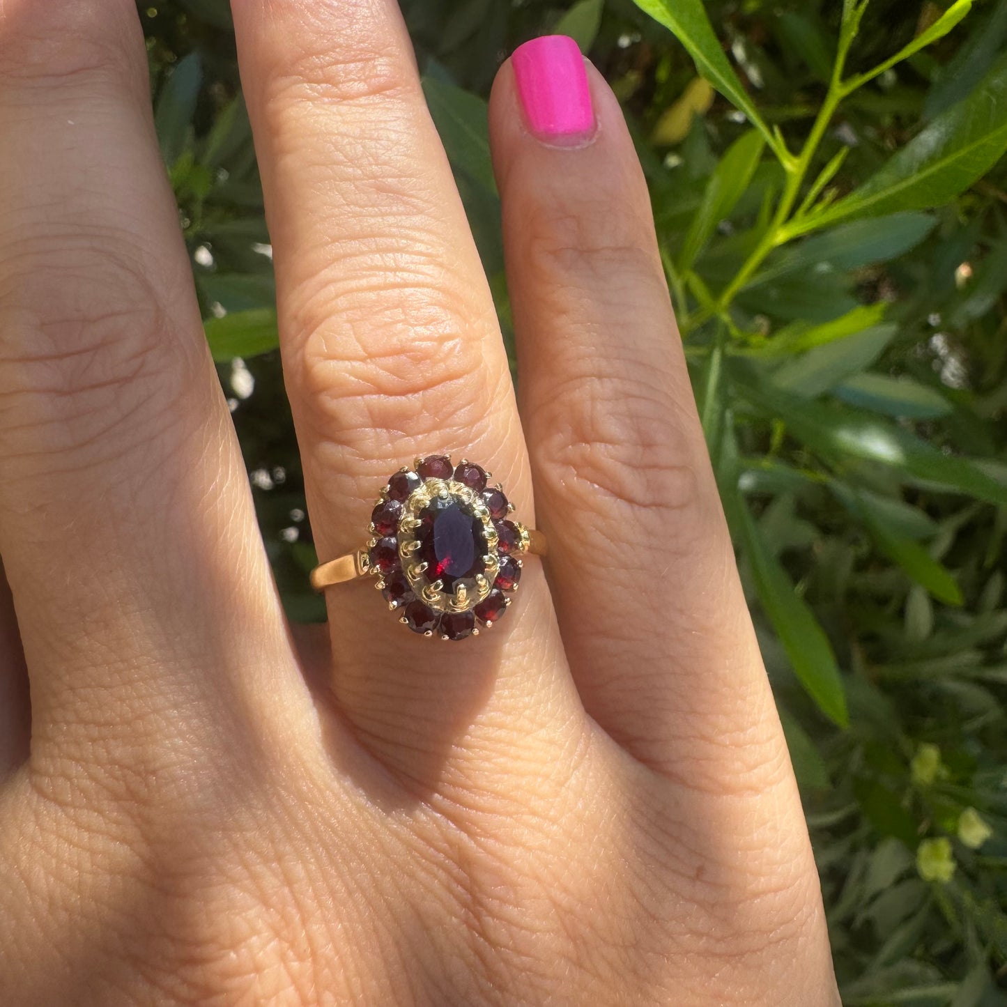 18K gold ring set with an oval garnet center stone, surrounded by smaller garnets