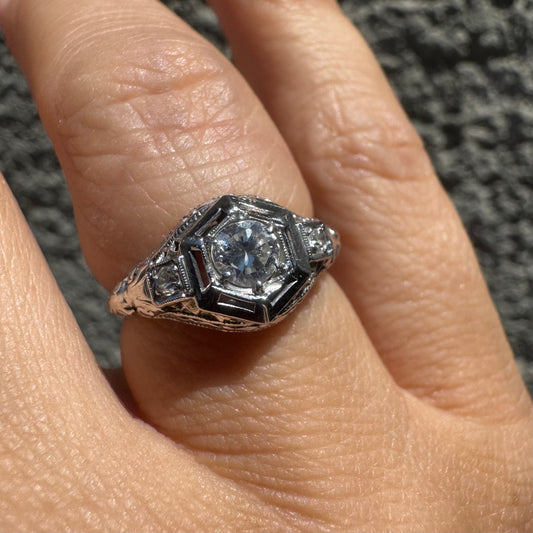 14K gold ring set with a central round diamond, framed by geometric Art Deco details and additional accent stones.