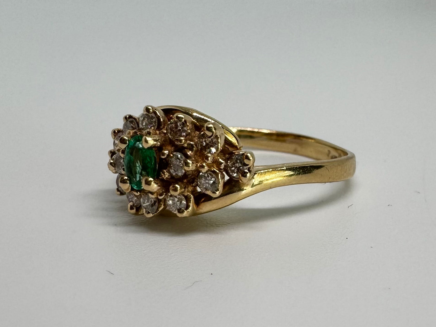 14K gold ring set with Emerald at its center, surrounded by a halo of brilliant-cut diamonds arranged in a floral-inspired cluster