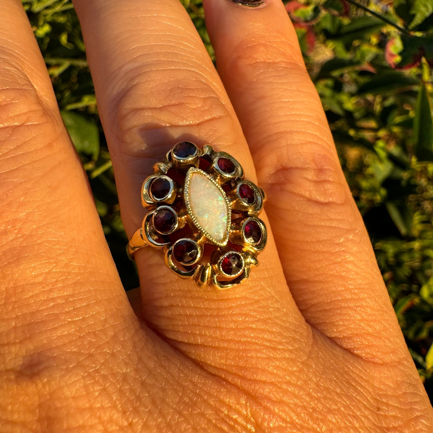 14K gold ring set with a luminous marquise-cut Opal at the center, surrounded by deep red Garnet cabochons