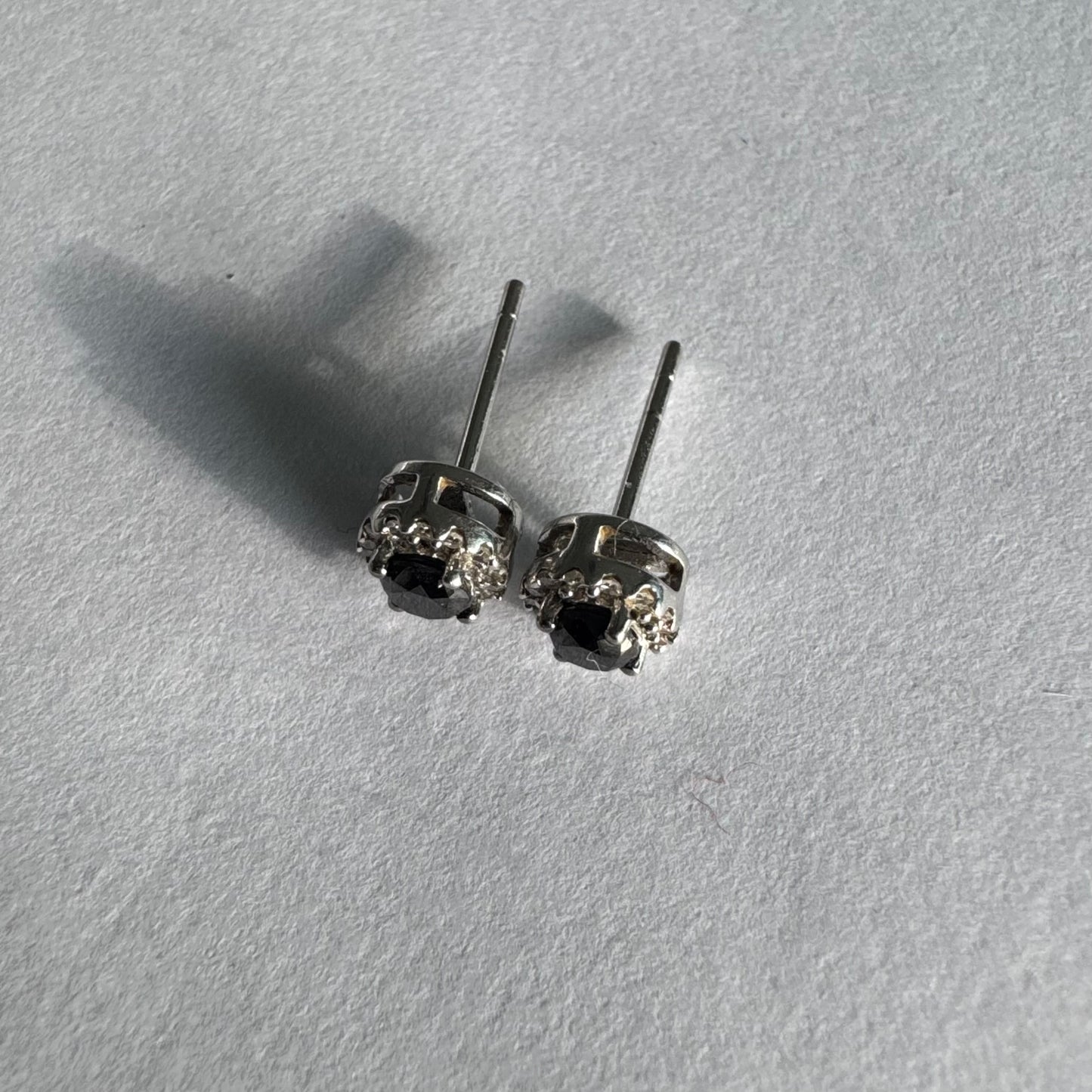 עגילי זהב לבן 10 קראט צמודים לאוזן, משובצים יהלומים שחורים עגולים במרכז ומסביבם הילה של יהלומים לבנים מנצנצים.