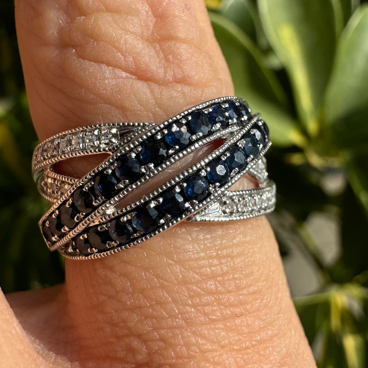 טבעת זהב לבן 14 קראט,קרוס, בעיצוב אלגנטי, משובצת בשורות של ספירים כחולים עמוקים ויהלומים מנצנצים.