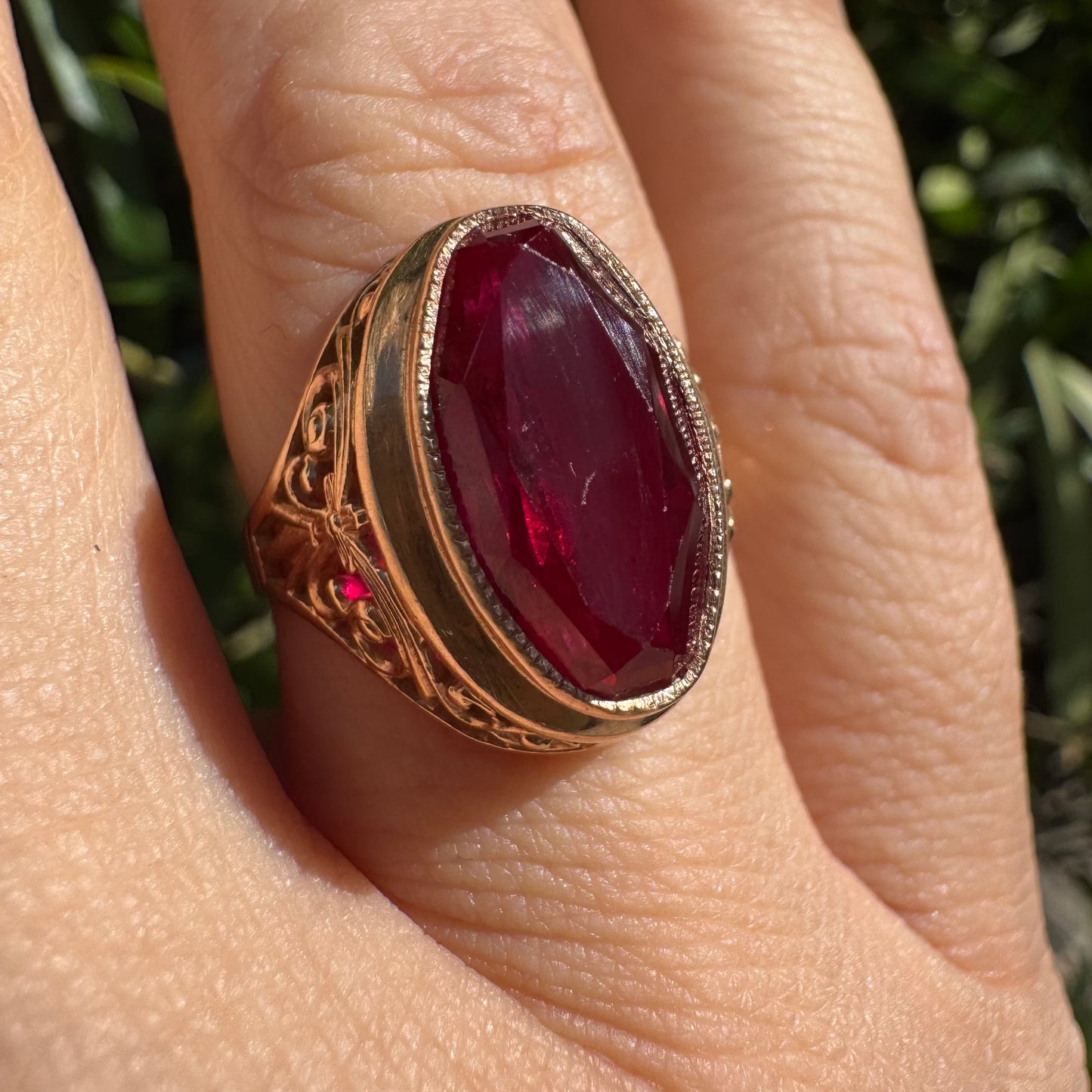 14K gold ring crowned with a vivid oval-cut Ruby, framed in an ornate bezel and accented by intricate filigree details