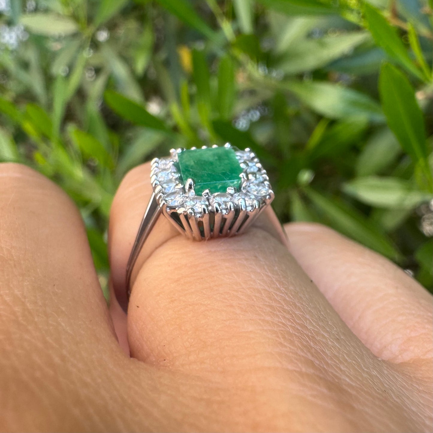 18K gold ring set with a green Emerald at the center, surrounded by a halo of sparkling round Diamonds.