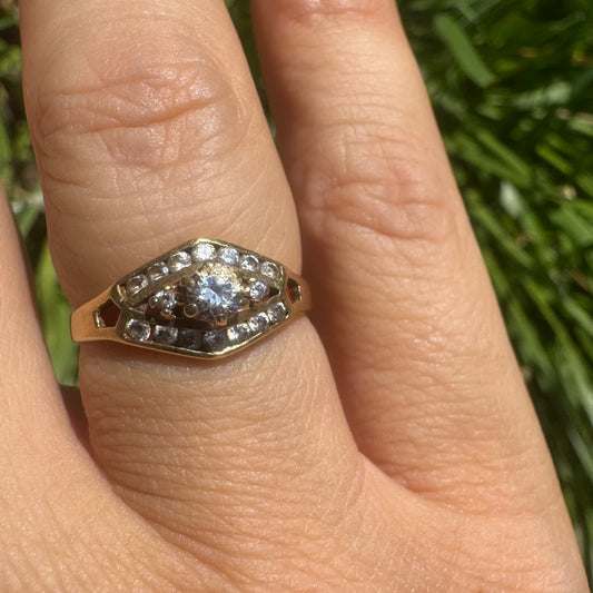 18K gold ring set with a central round Diamond, surrounded by rows of Diamonds in a decorative setting.