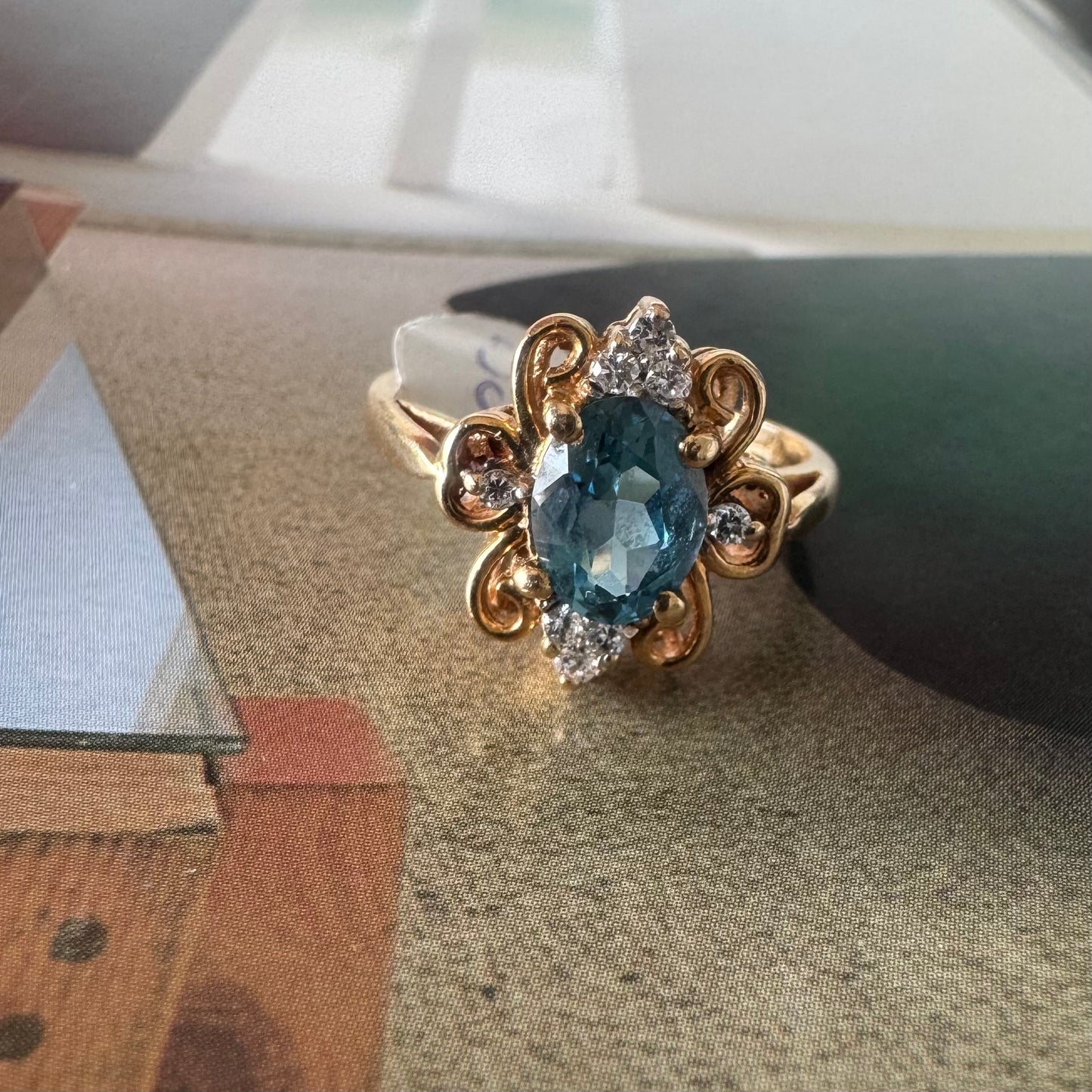 18K gold ring featuring an oval-cut Blue Topaz at the center, accented by sparkling side Diamonds and elegant scroll details.
