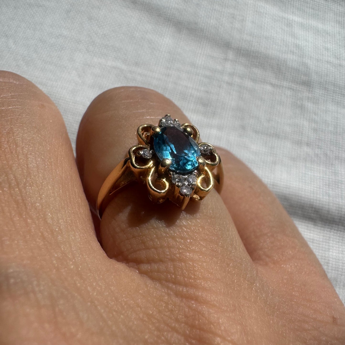 18K gold ring featuring an oval-cut Blue Topaz at the center, accented by sparkling side Diamonds and elegant scroll details.