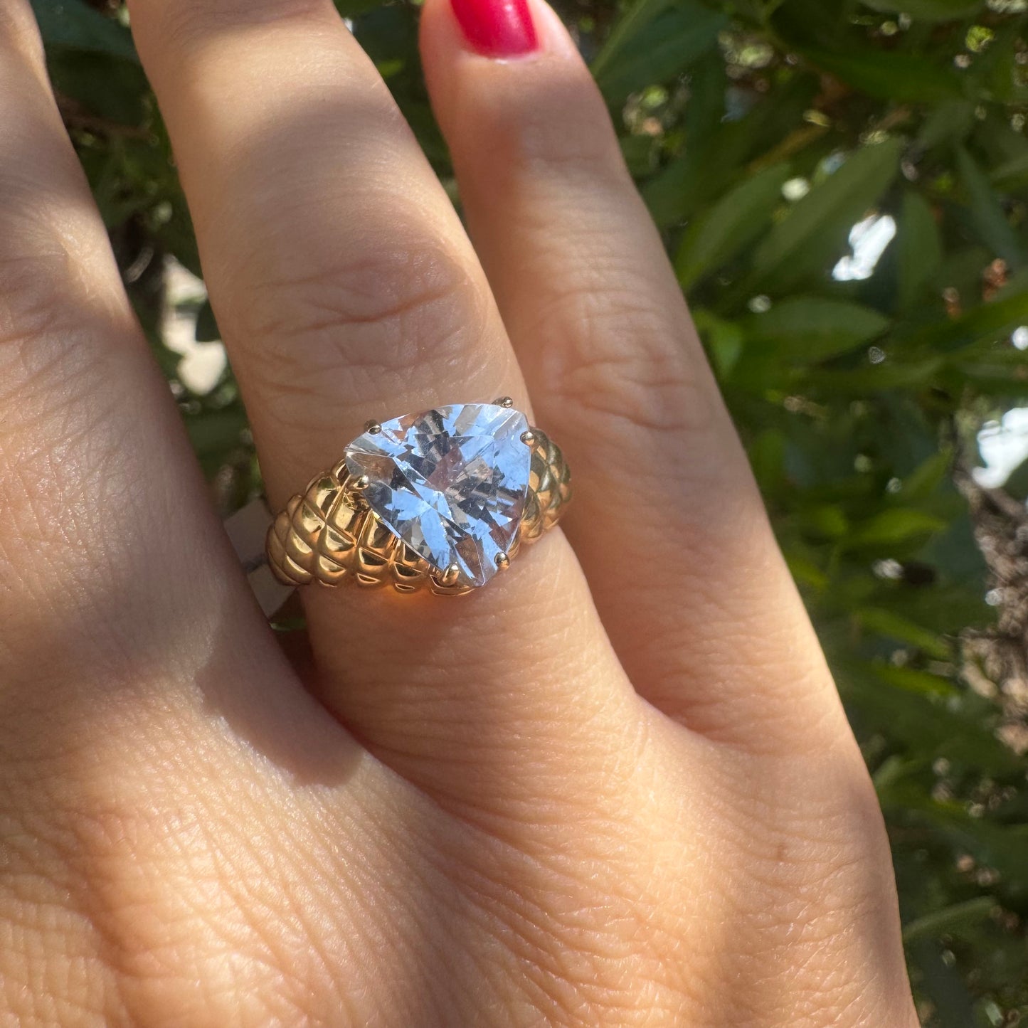 טבעת זהב צהוב 10 קראט משובצת אבן שקופה גדולה בחיתוך משולש, עם טבעת בעלת טקסטורה ייחודית ובולטת.