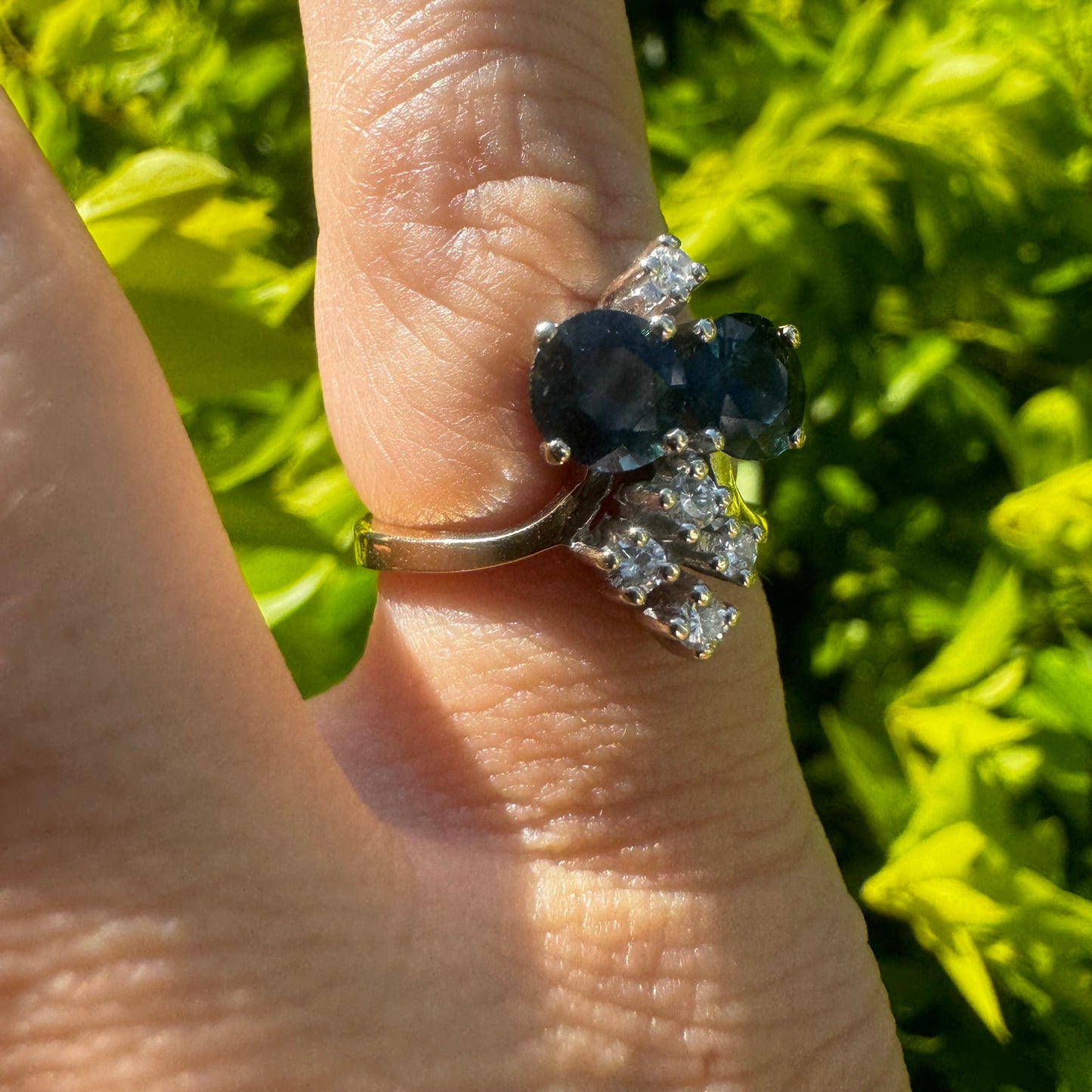 14K gold ring set with two deep blue oval Sapphires accented by clusters of brilliant white Diamonds.