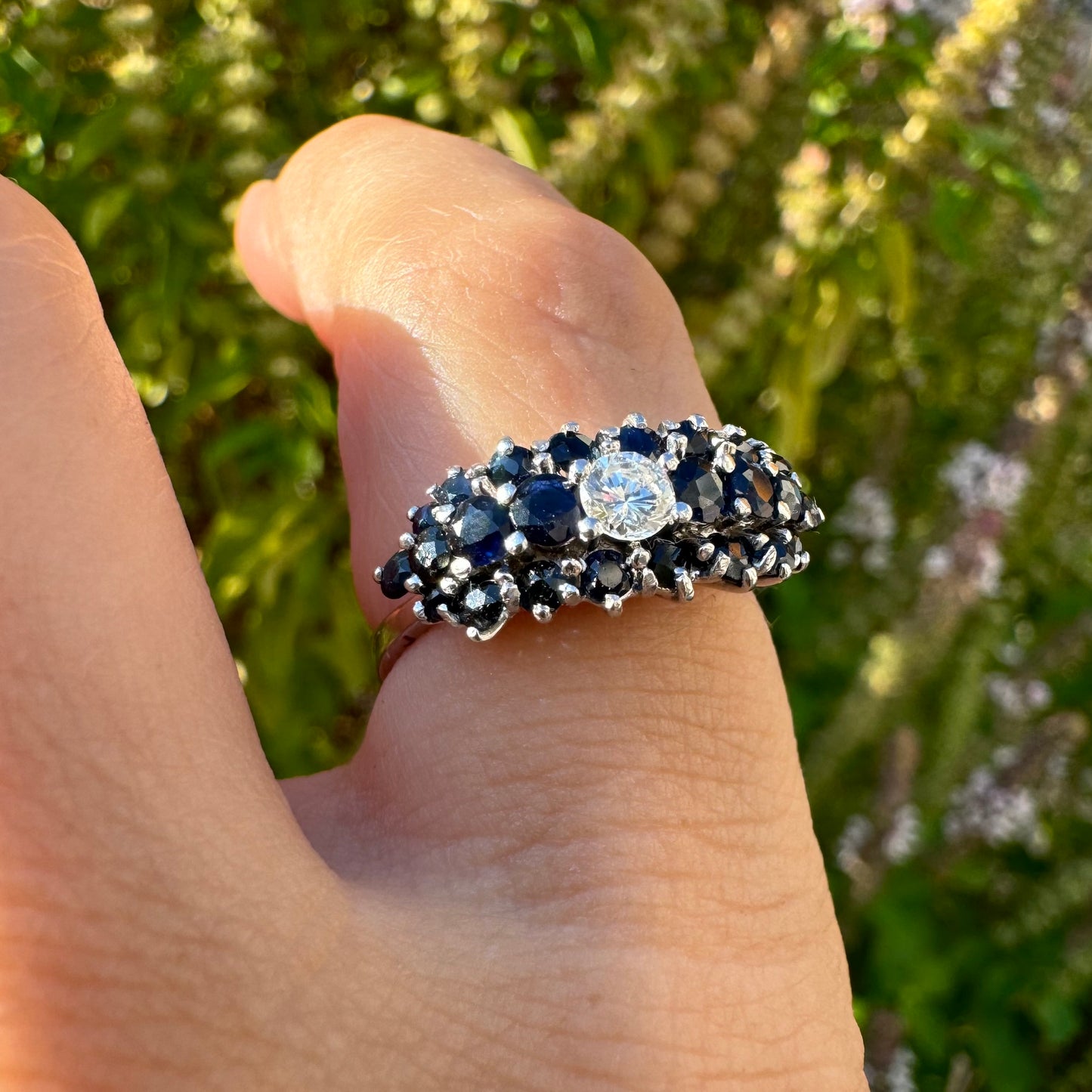 18K gold ring set with a brilliant-cut central Diamond, surrounded by a striking cluster of deep blue Sapphires.