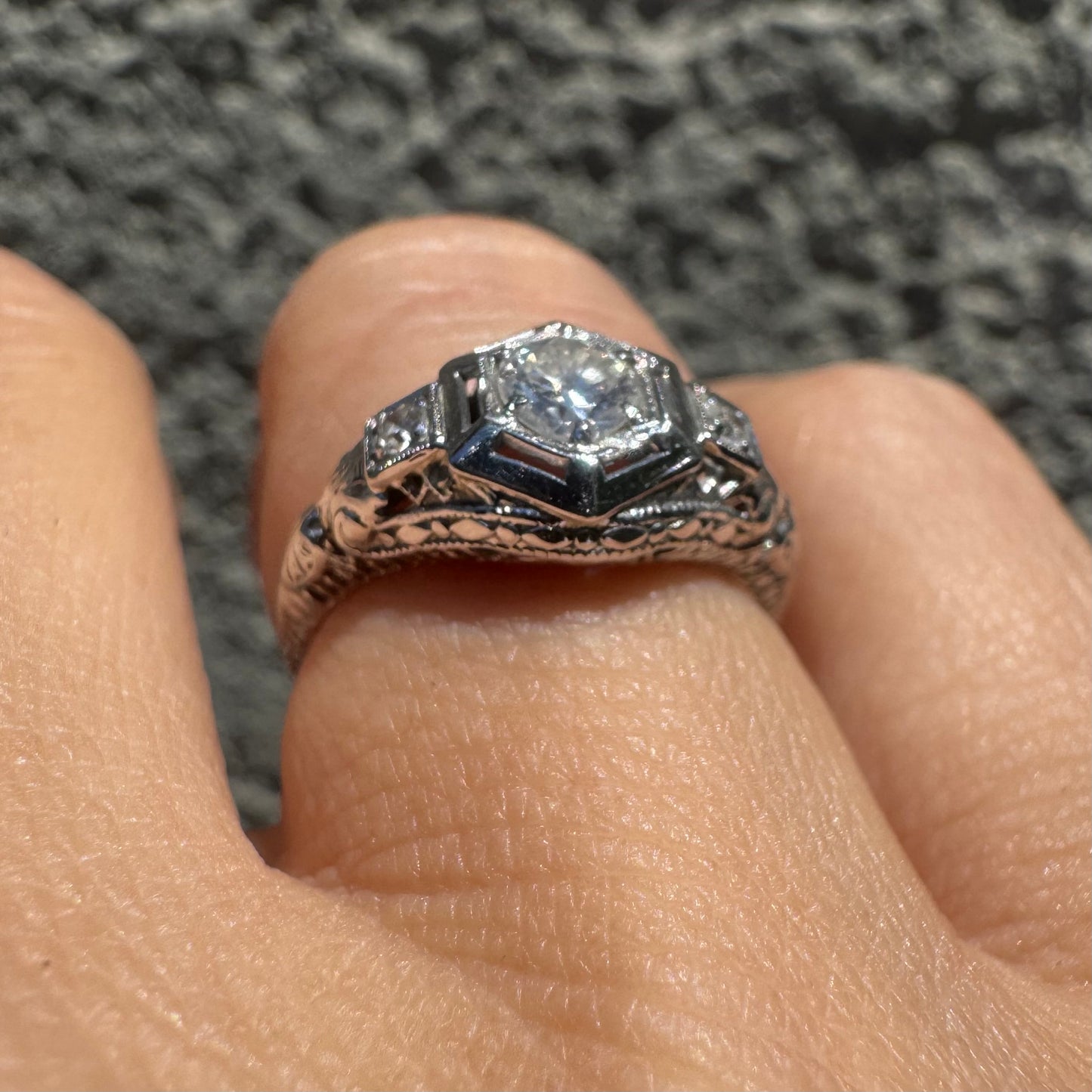 14K gold ring set with a central round diamond, framed by geometric Art Deco details and additional accent stones.