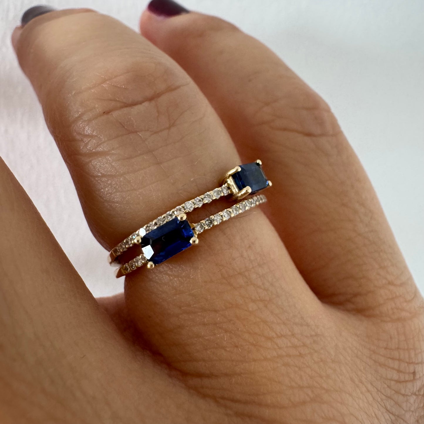 טבעת זהב צהוב 14 קראט בעיצוב פתוח, משובצת שתי אבני ספיר בחיתוך אמרלד ושורות יהלומים עדינים.