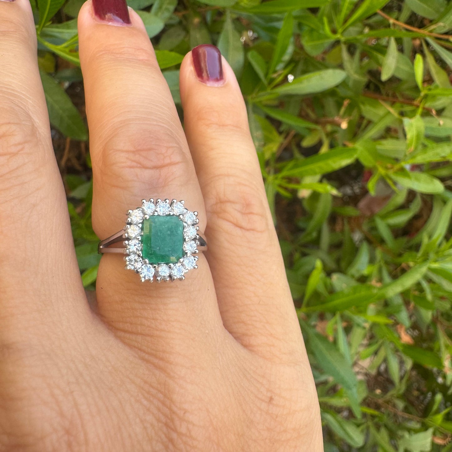 18K gold ring set with a green Emerald at the center, surrounded by a halo of sparkling round Diamonds.