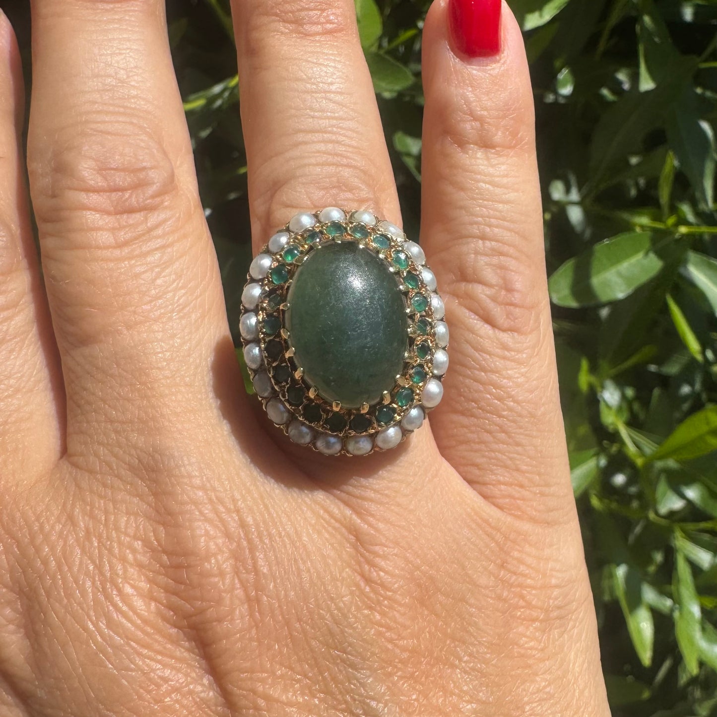 14K gold set with a large oval green Jade at its center, surrounded by concentric halos of sparkling Emeralds and delicate pearls
