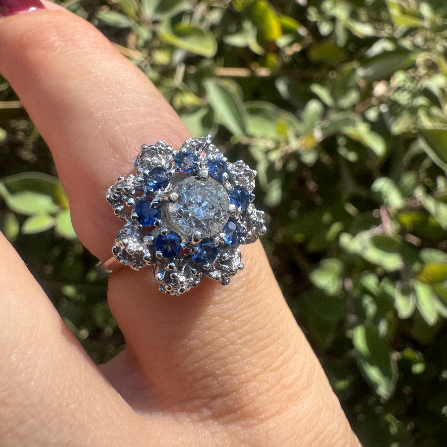 18K gold ring featuring a large round Diamond at the center, surrounded by a floral halo of purple -blue Tanzanite and & Diamonds.