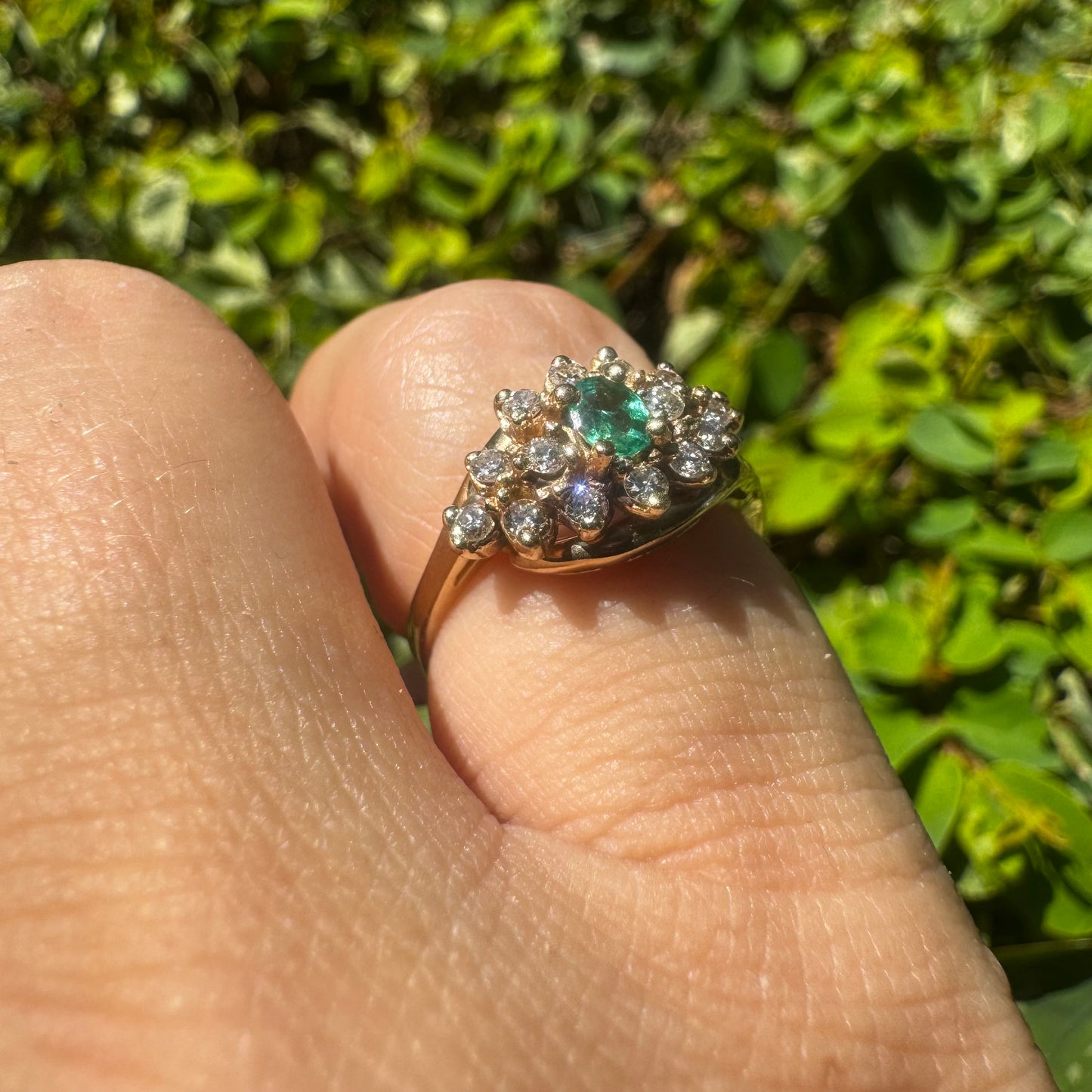 14K gold ring set with Emerald at its center, surrounded by a halo of brilliant-cut diamonds arranged in a floral-inspired cluster