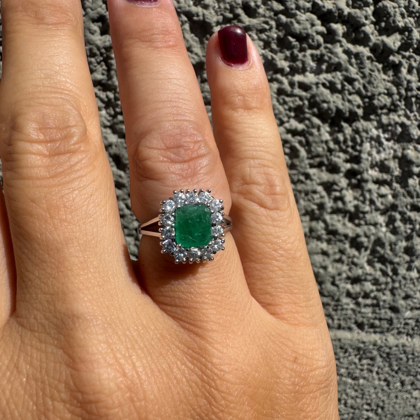 18K gold ring set with a green Emerald at the center, surrounded by a halo of sparkling round Diamonds.