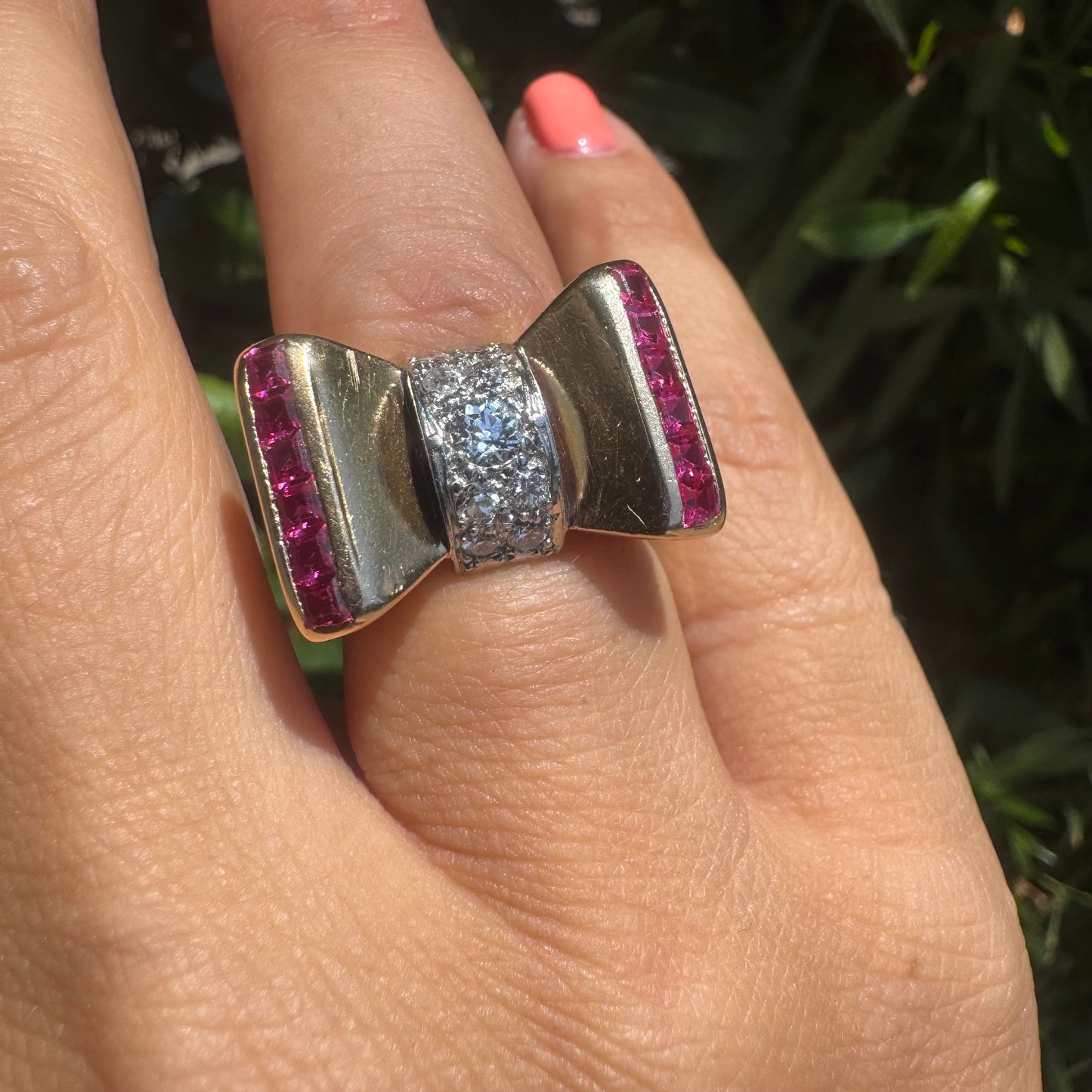 18K gold bow-shaped ring set with pavé Diamonds at the center and rows of square-cut Rubies on the sides.