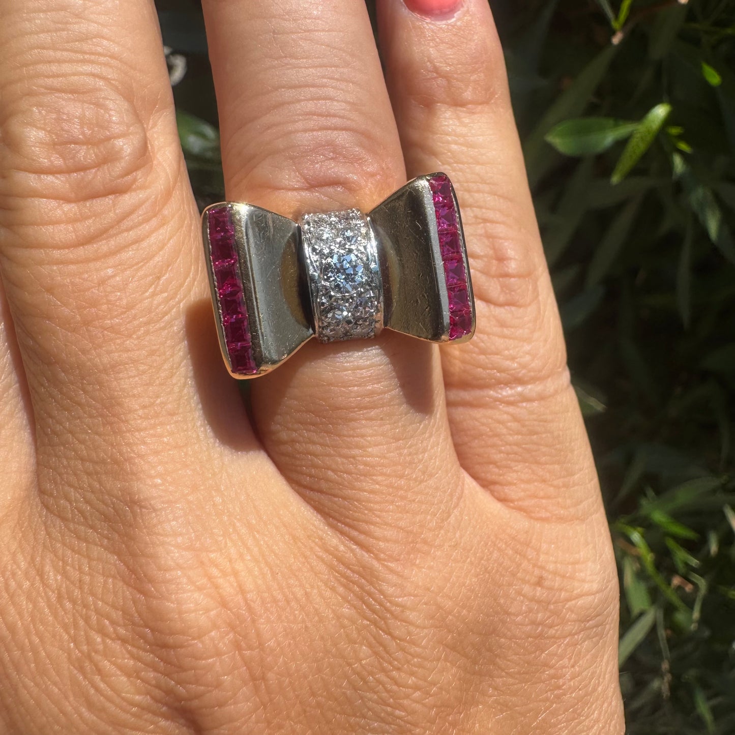 18K gold bow-shaped ring set with pavé Diamonds at the center and rows of square-cut Rubies on the sides.