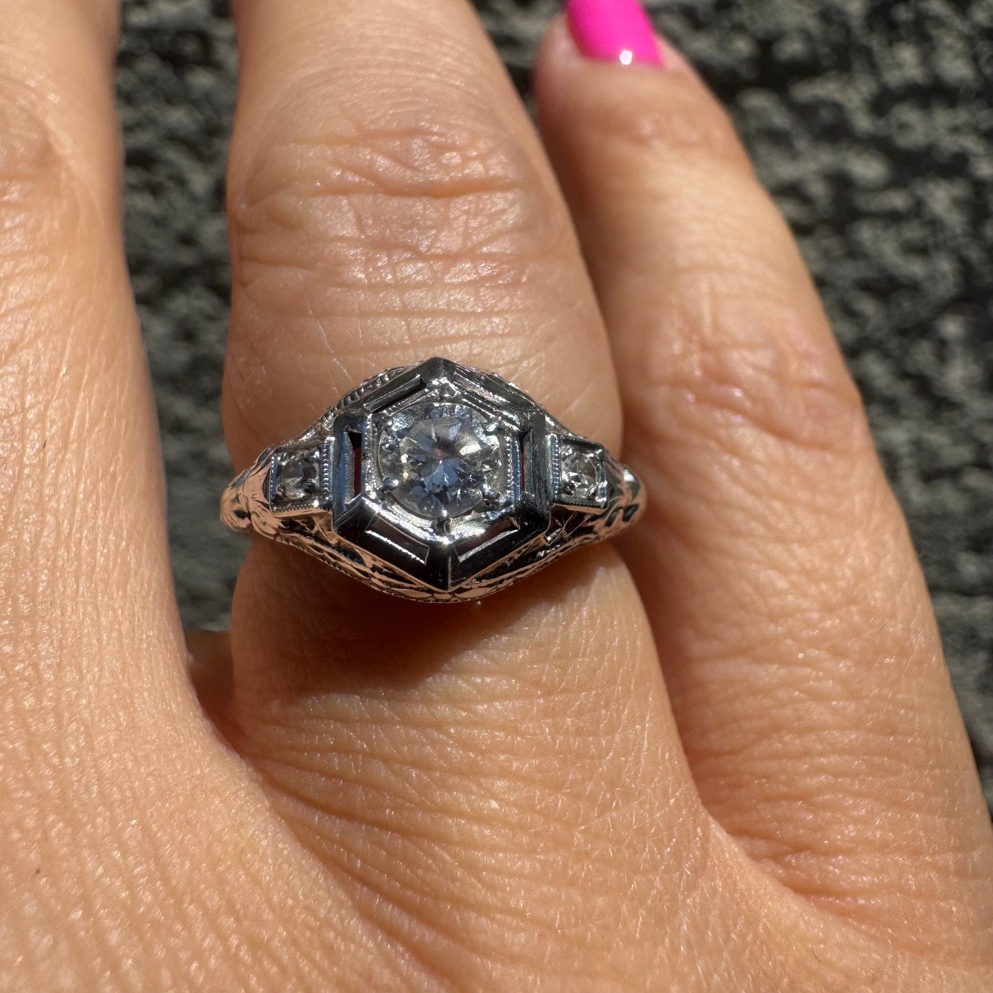 14K gold ring set with a central round diamond, framed by geometric Art Deco details and additional accent stones.