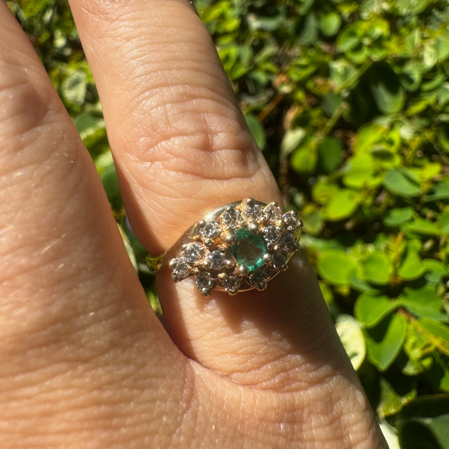 14K gold ring set with Emerald at its center, surrounded by a halo of brilliant-cut diamonds arranged in a floral-inspired cluster