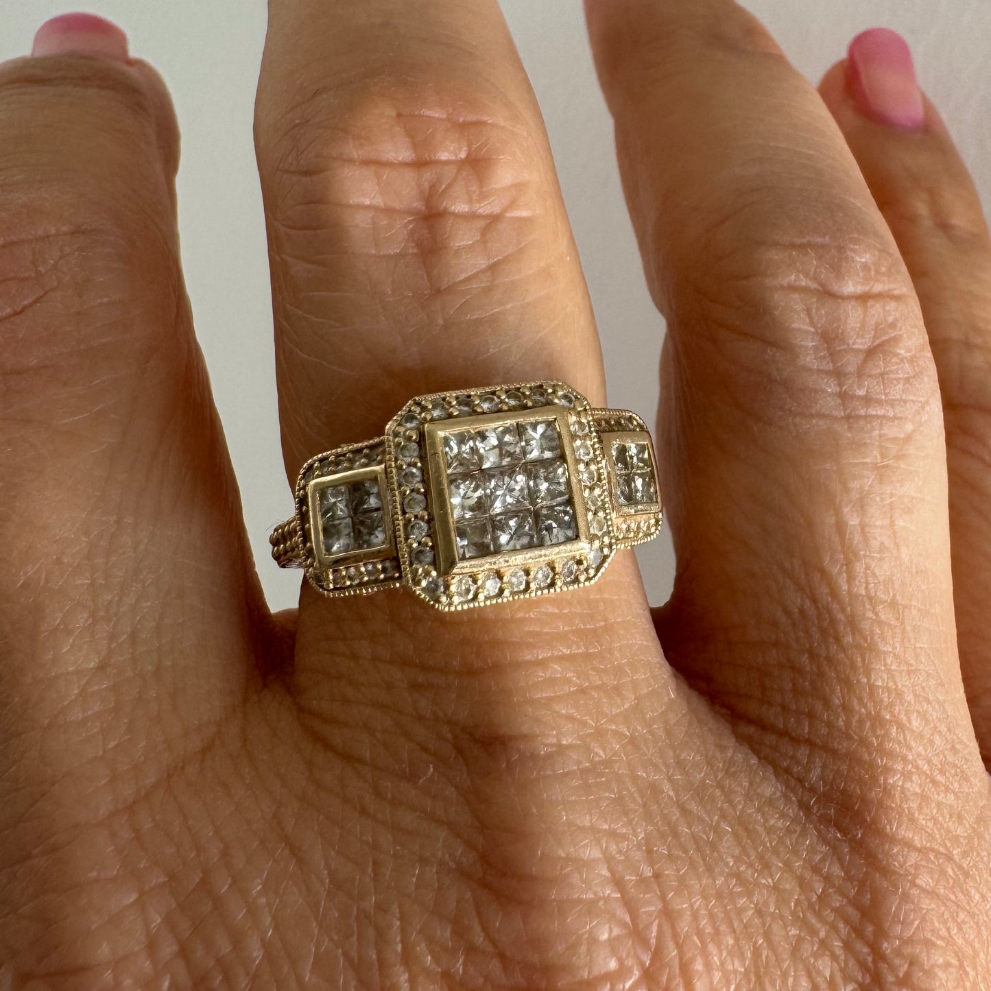 טבעת זהב צהוב 14 קראט משובצת יהלומים בחיתוך פרינסס במרכז, מוקפת הילה של יהלומים צדדיים.