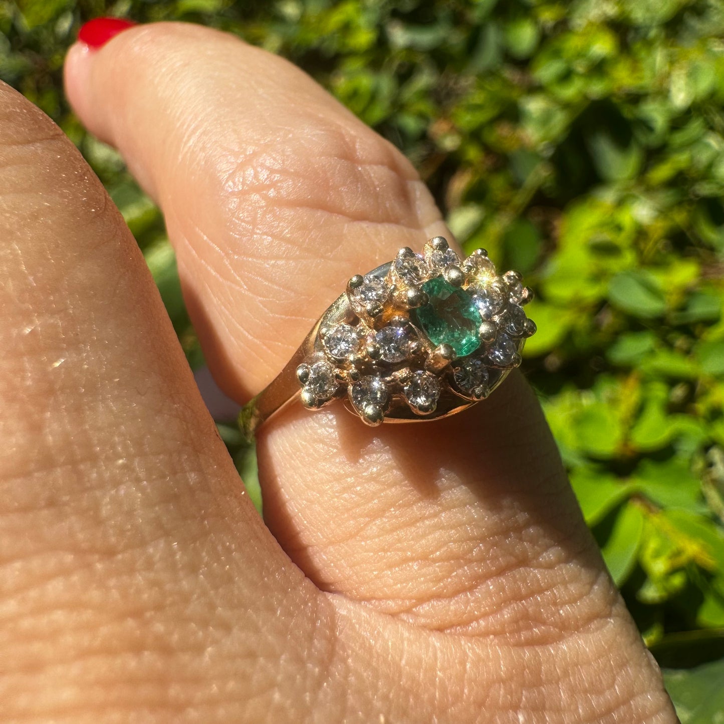 14K gold ring set with Emerald at its center, surrounded by a halo of brilliant-cut diamonds arranged in a floral-inspired cluster