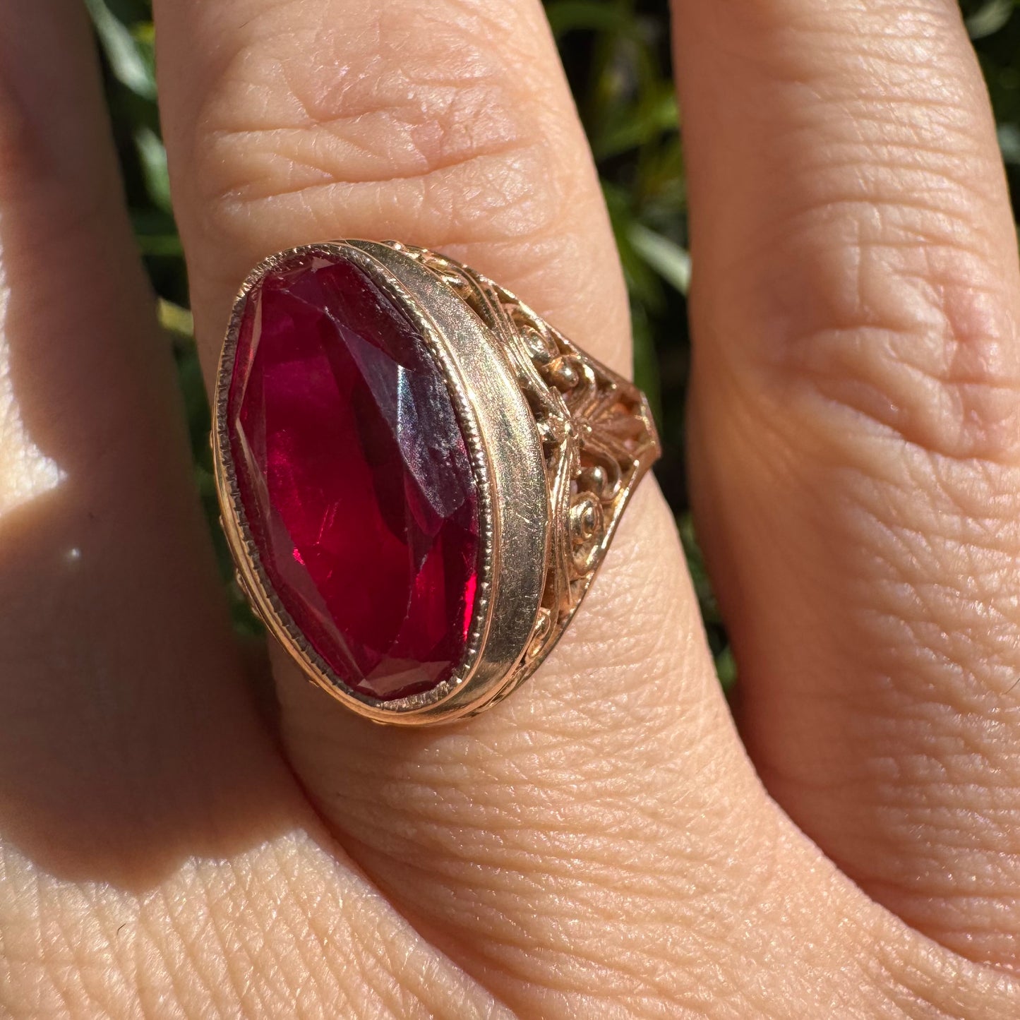 14K gold ring crowned with a vivid oval-cut Ruby, framed in an ornate bezel and accented by intricate filigree details