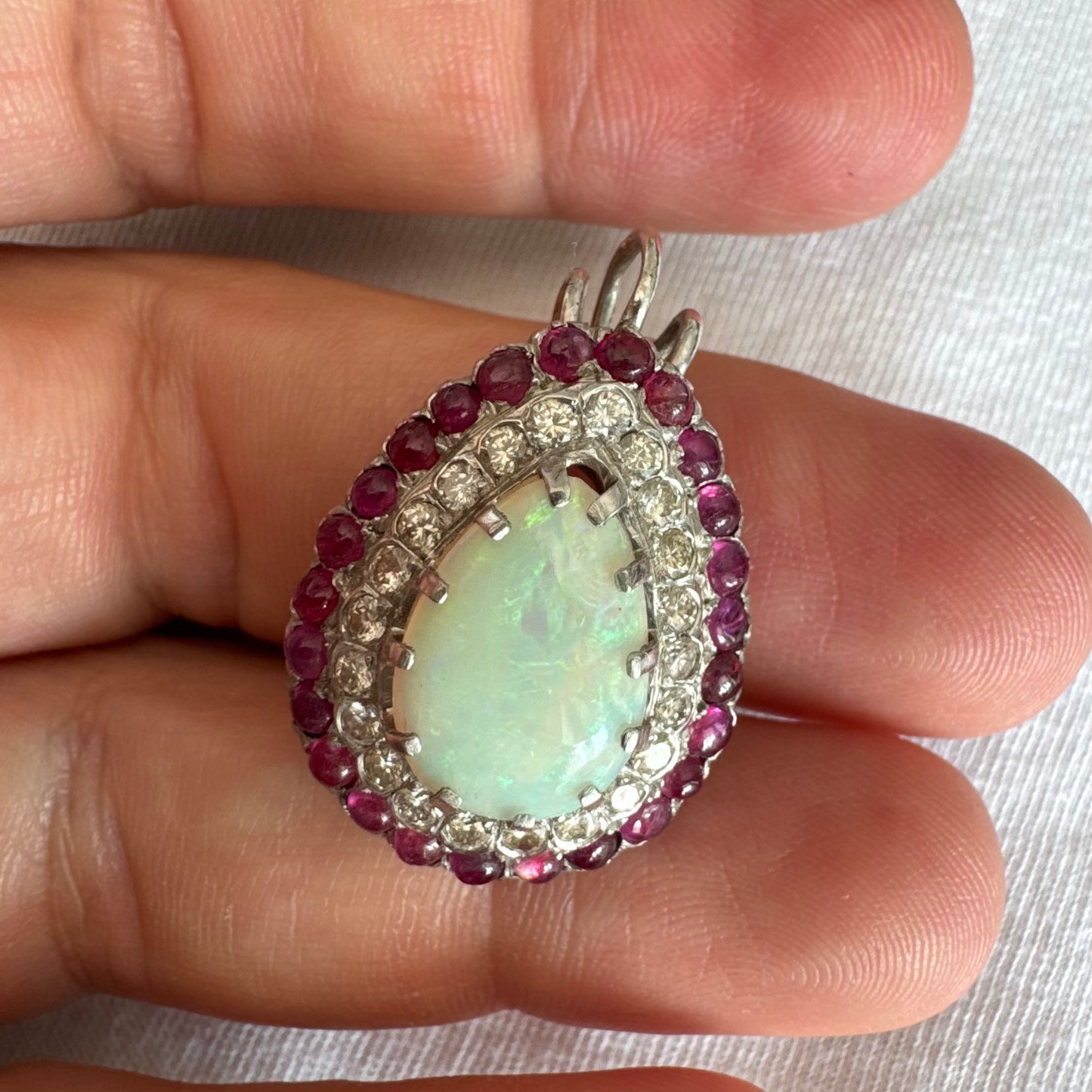 תליון זהב 14 קראט משובץ אבן אופל בחיתוך טיפה, מוקפת בשתי מסגרות של יהלומים ורובי נוצצים.