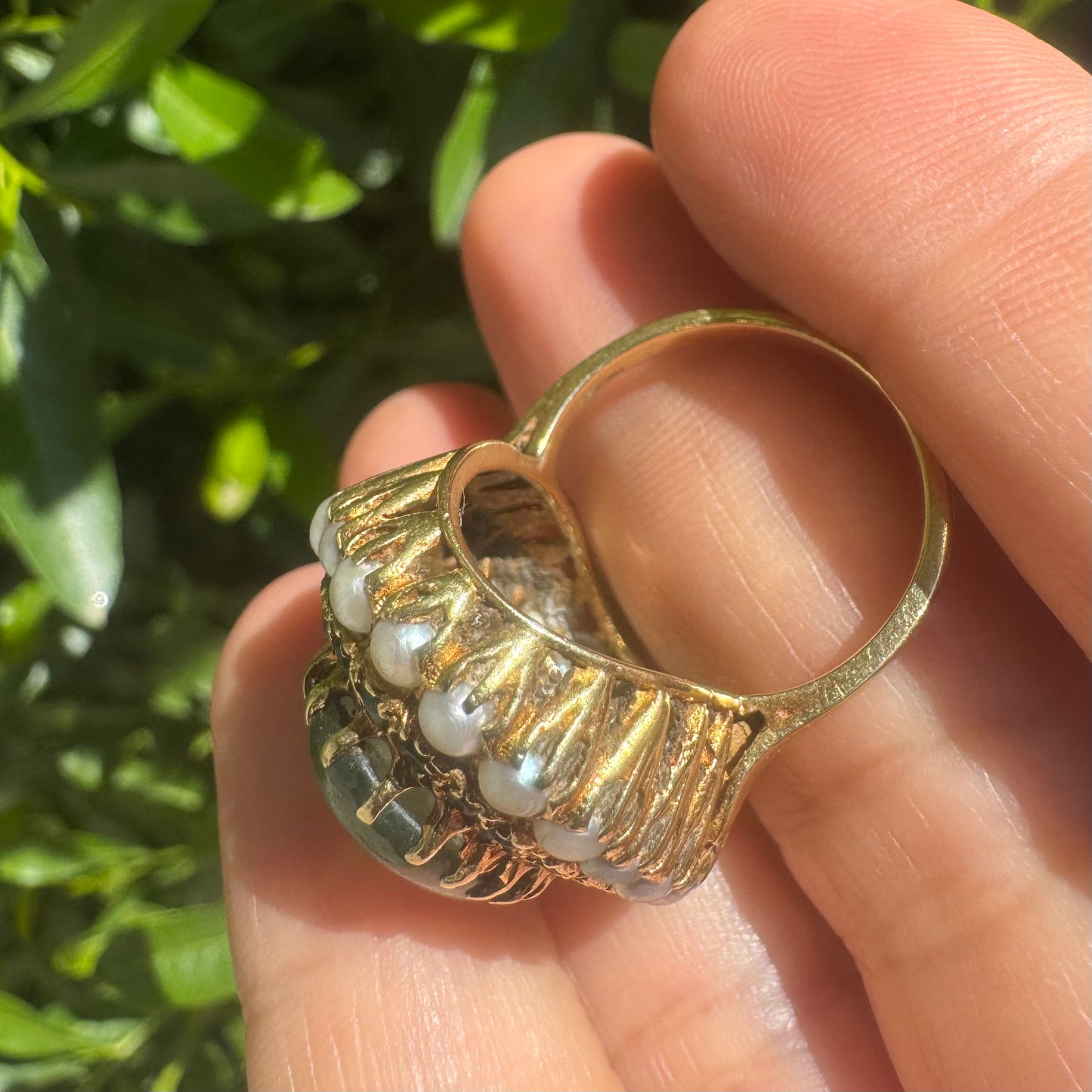 14K gold set with a large oval green Jade at its center, surrounded by concentric halos of sparkling Emeralds and delicate pearls