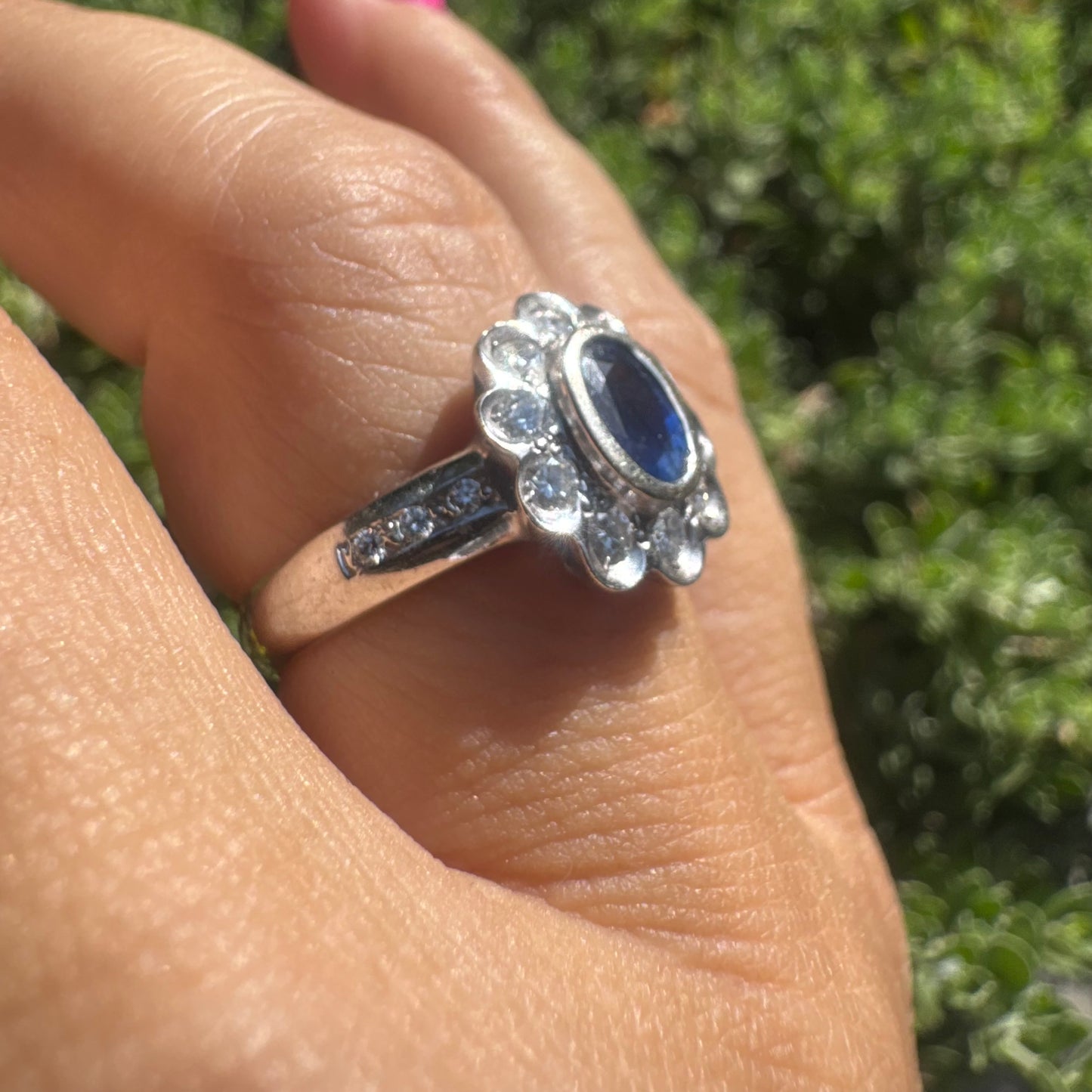 18K gold ring set with an oval blue Sapphire surrounded by a halo of round Diamonds in a flower-shaped design.