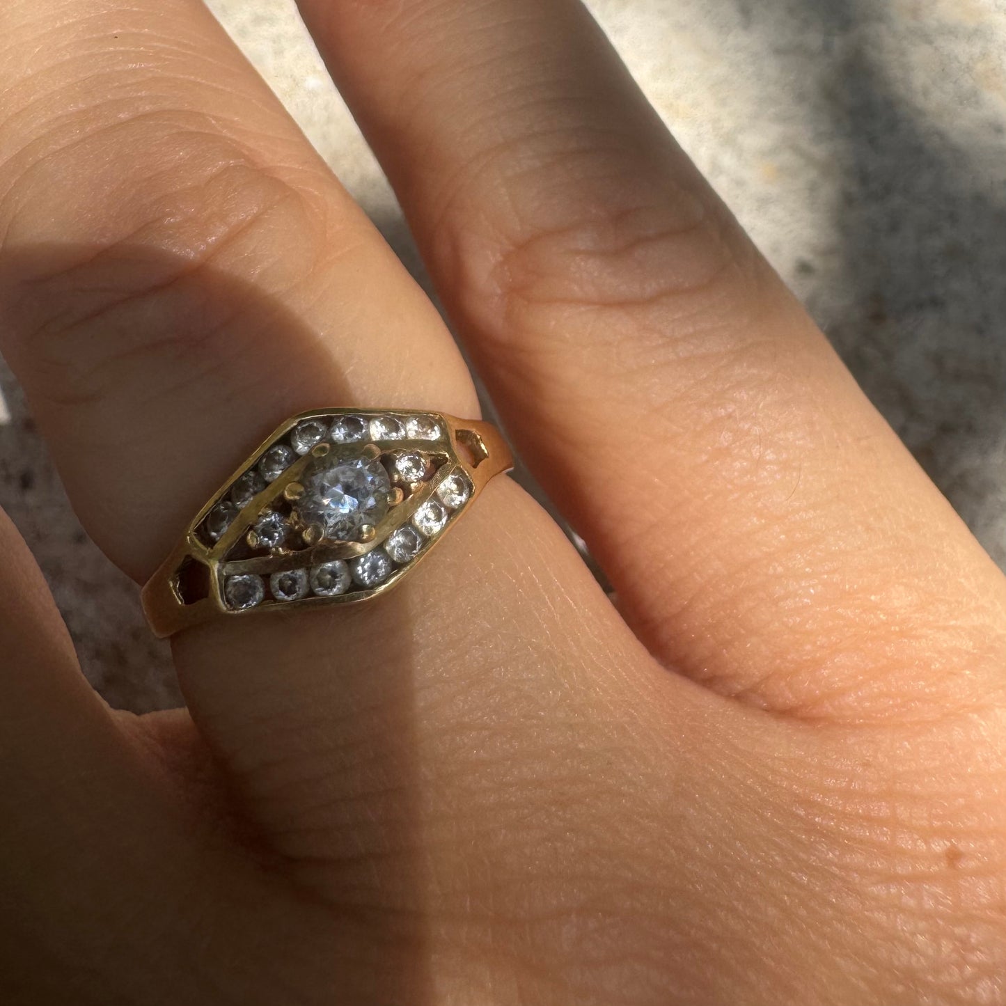 18K gold ring set with a central round Diamond, surrounded by rows of Diamonds in a decorative setting.