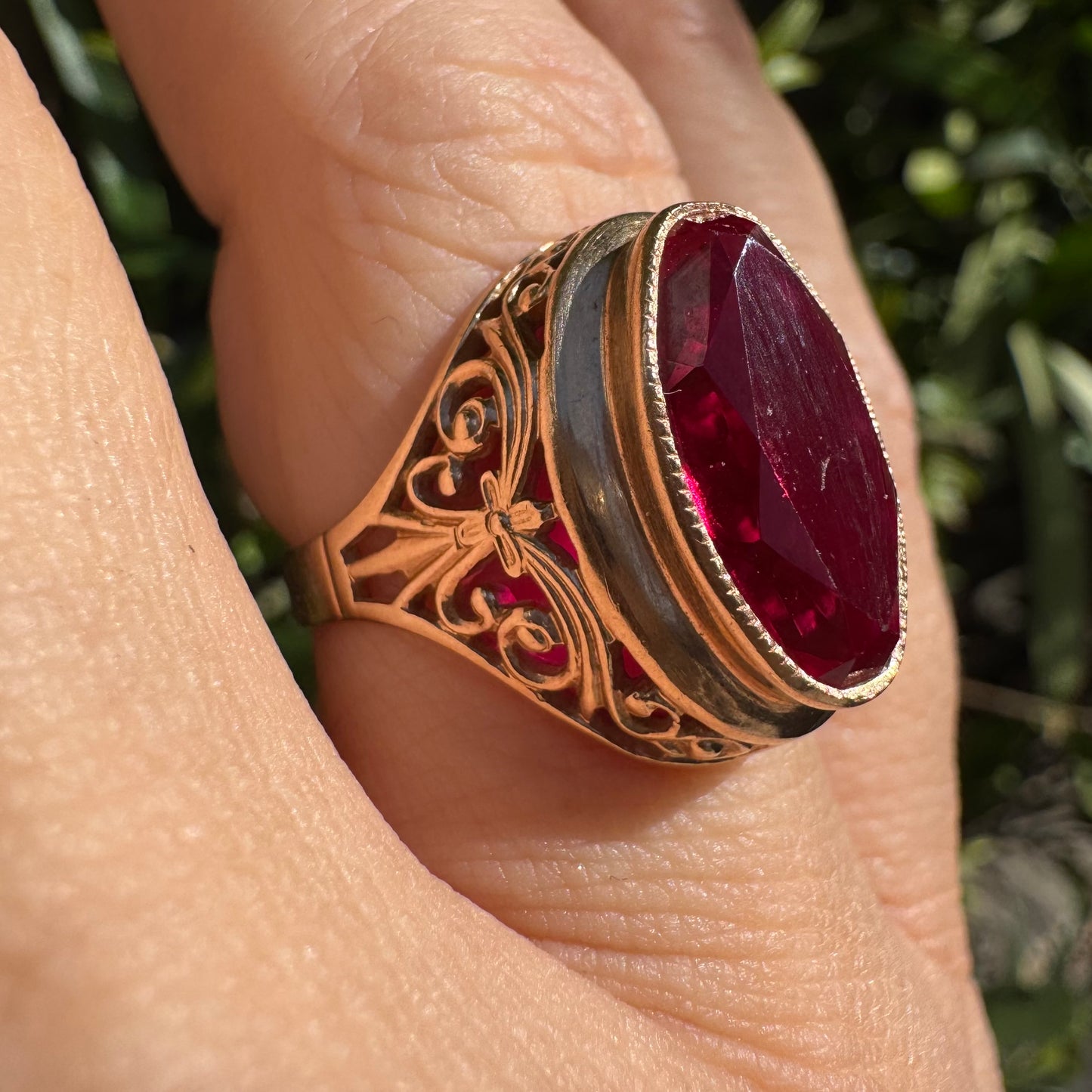 14K gold ring crowned with a vivid oval-cut Ruby, framed in an ornate bezel and accented by intricate filigree details