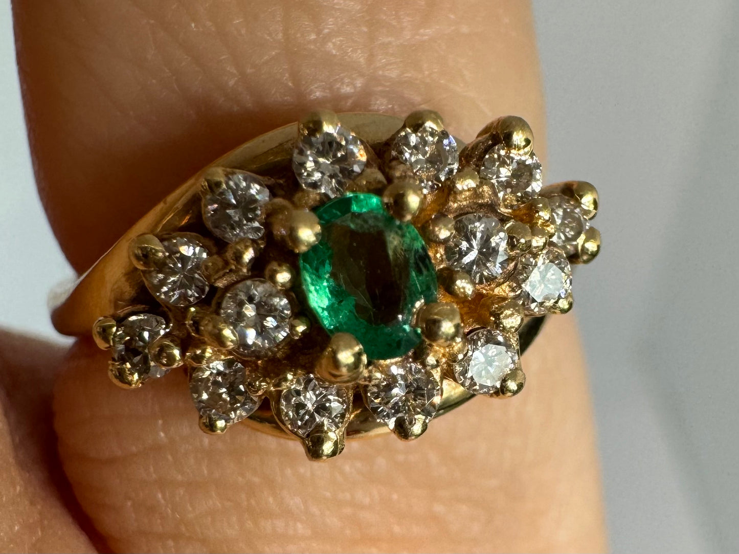 14K gold ring set with Emerald at its center, surrounded by a halo of brilliant-cut diamonds arranged in a floral-inspired cluster