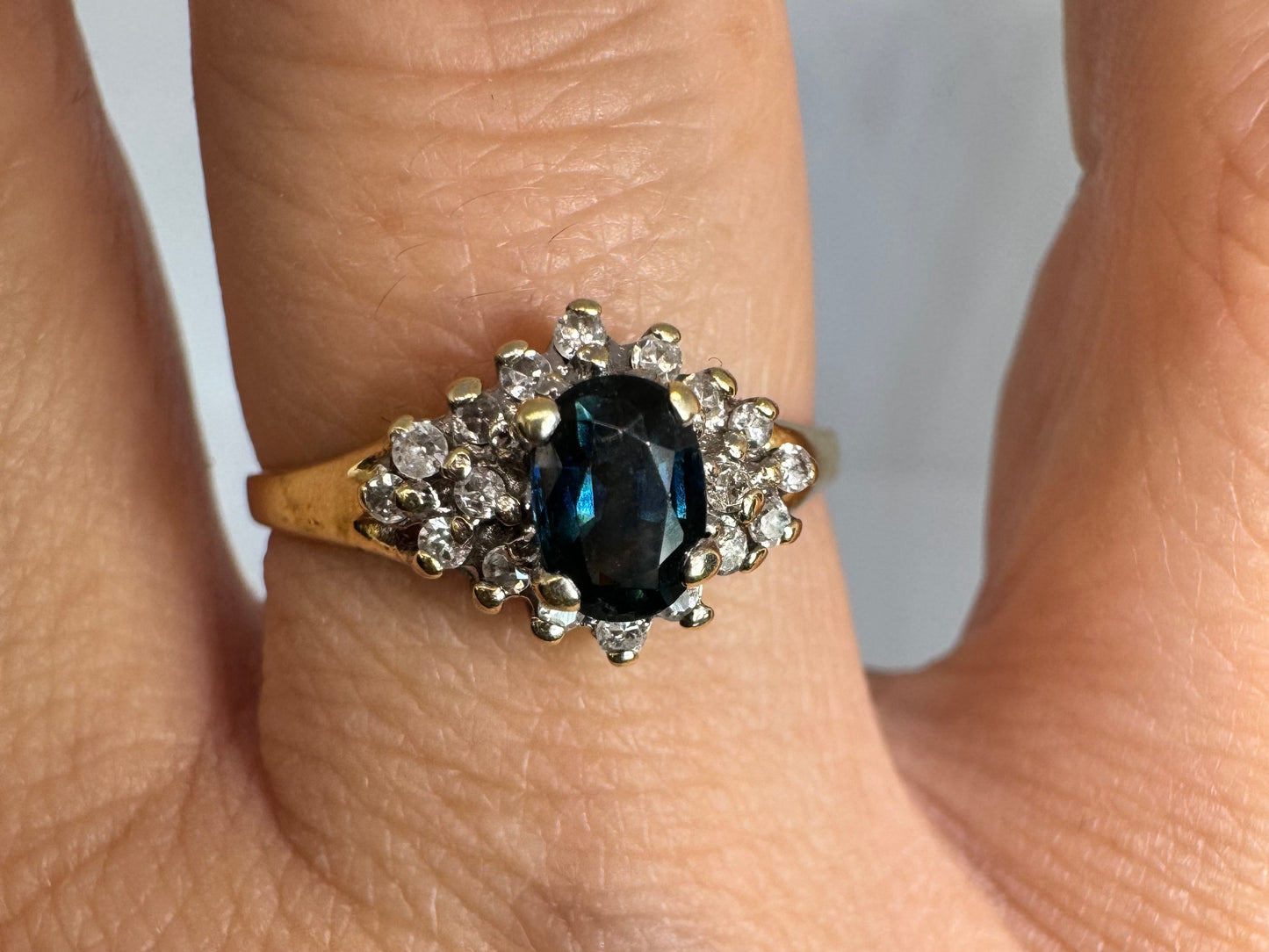 14K gold ring set with an oval blue Sapphire surrounded by sparkling Diamonds