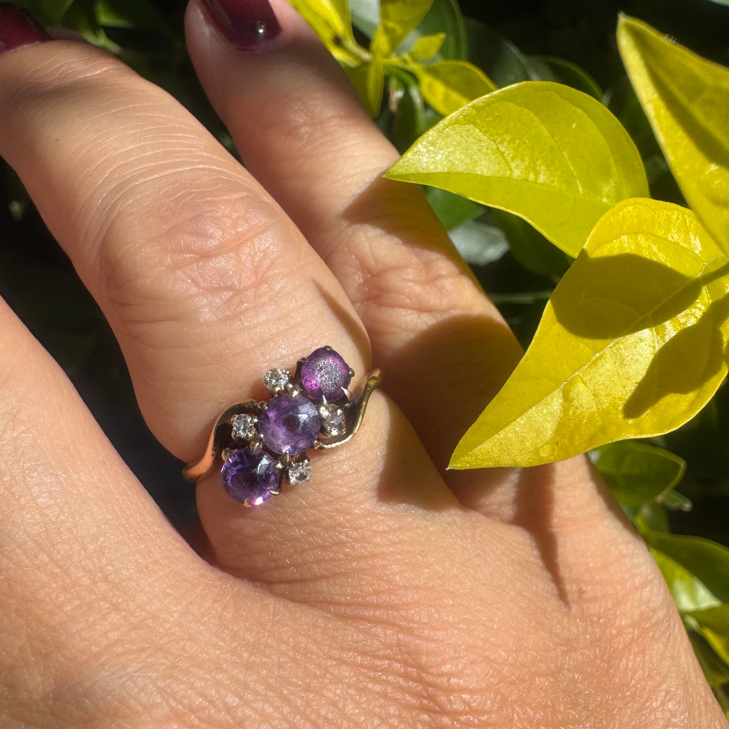 14K gold ring set with three round purple amethysts, accented by small sparkling Diamonds.