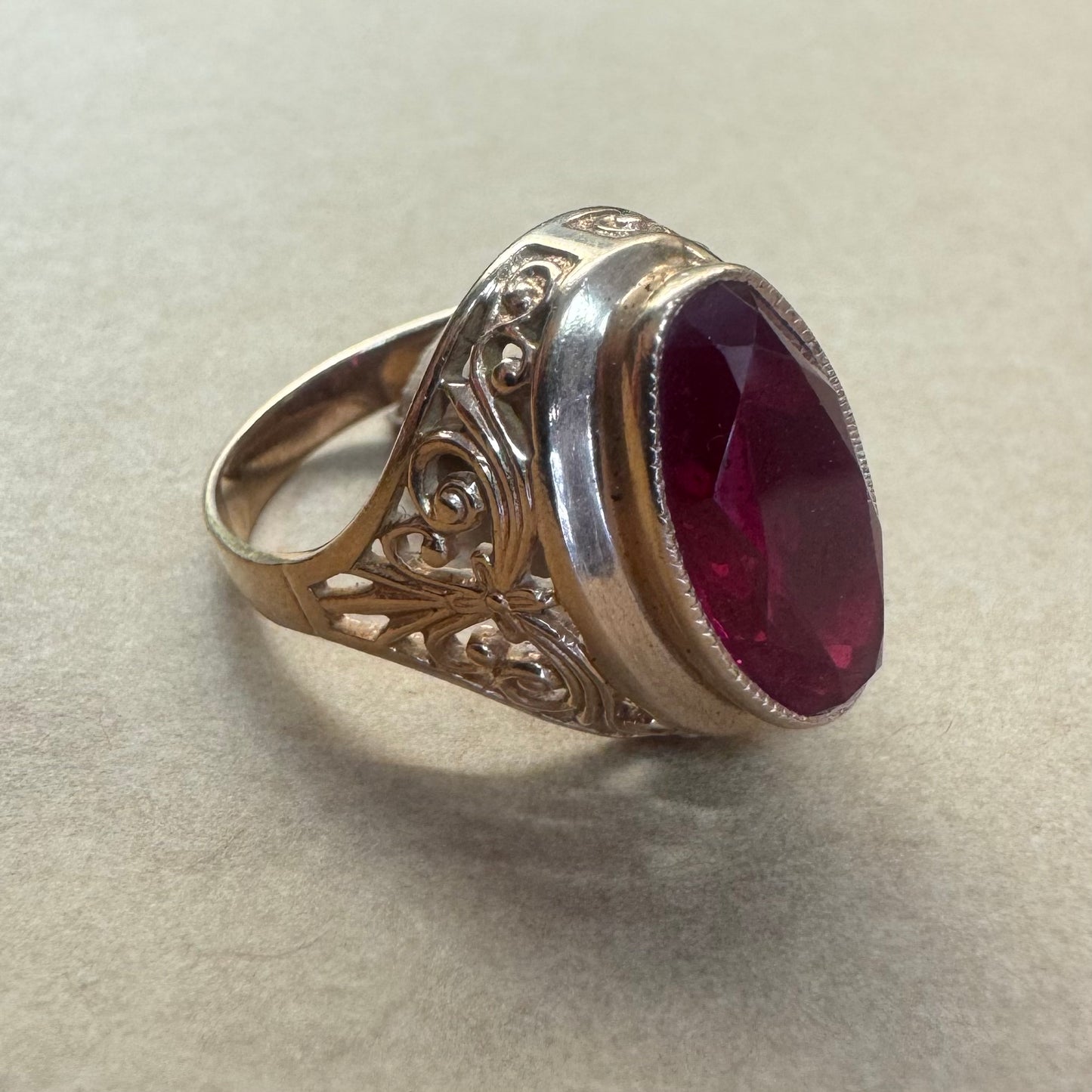 14K gold ring crowned with a vivid oval-cut Ruby, framed in an ornate bezel and accented by intricate filigree details