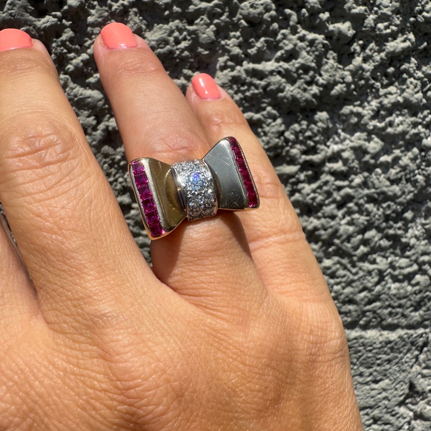 18K gold bow-shaped ring set with pavé Diamonds at the center and rows of square-cut Rubies on the sides.